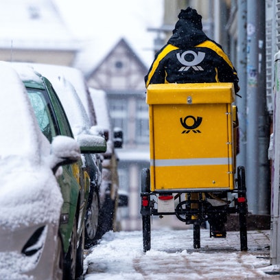 Eine Briefträgerin ist mit ihrem Fahrrad bei starkem Schneefall unterwegs.