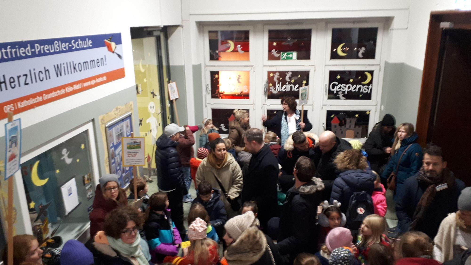 Ein Schulfoyer gefüllt mit Kindern und Erwachsenen ist zu sehen.