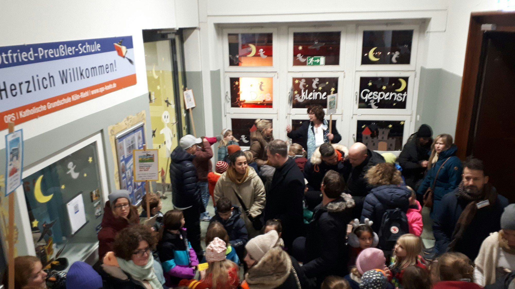 Ein Schulfoyer gefüllt mit Kindern und Erwachsenen ist zu sehen.