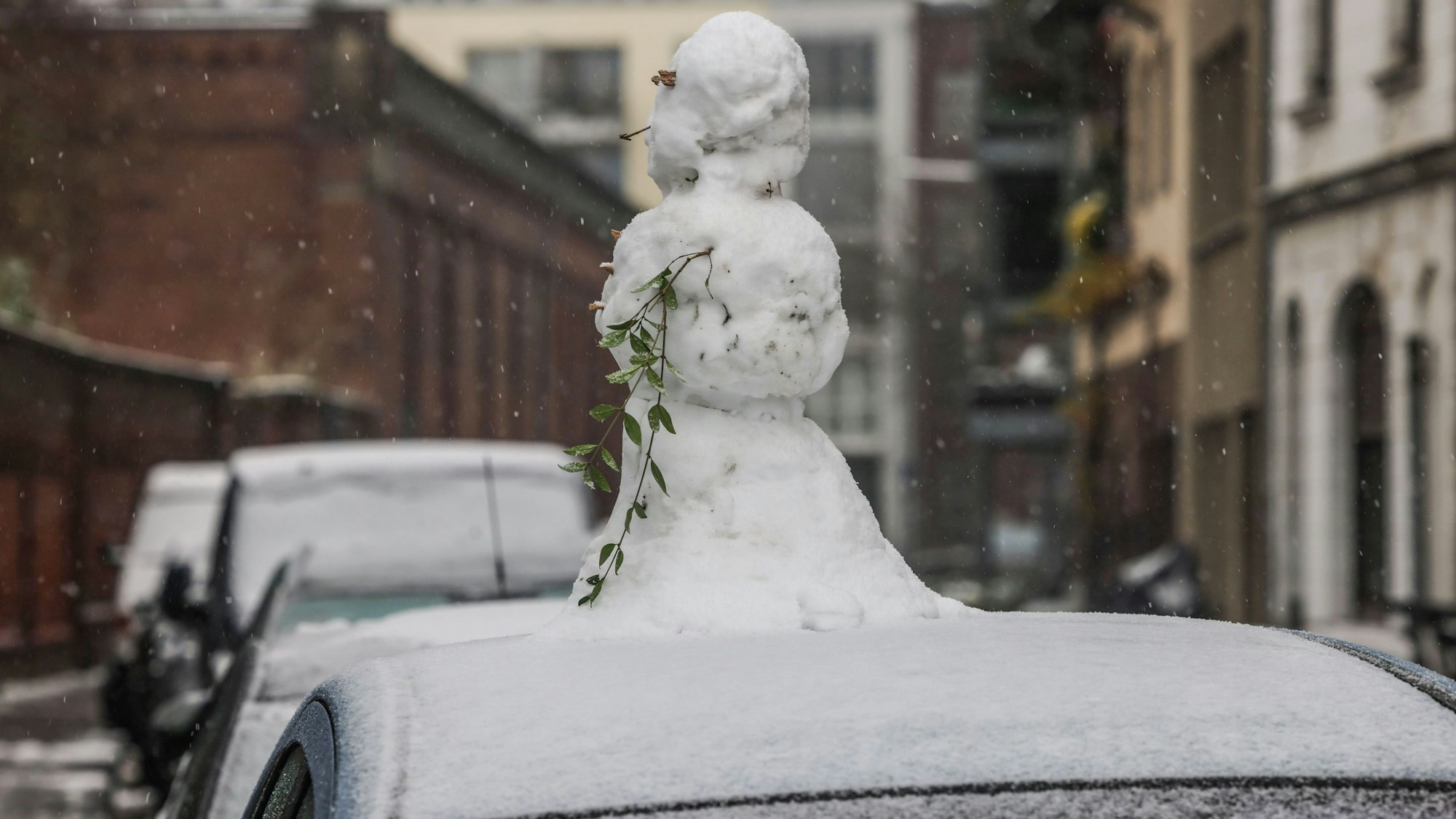 Ein Schneemann steht in Köln auf einem Autodach.