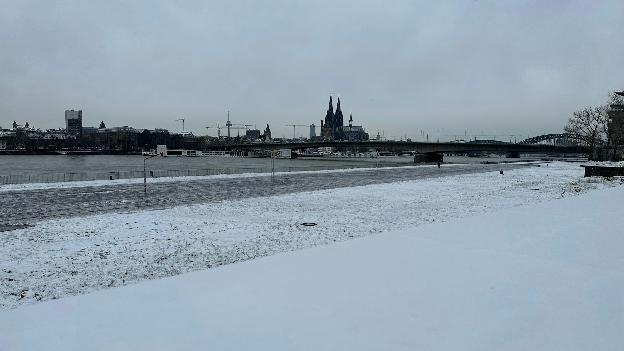 Am Montag, 4. Dezember, liegt noch eine leichte Schneedecke über einigen Teilen Kölns. Am Rhein sind Grünflächen mit Schnee bedeckt.