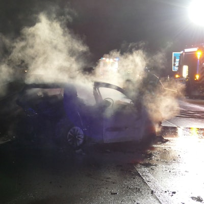 Das Foto zeigt den ausgebrannten Wagen und ein Einsatzfahrzeug der Feuerwehr auf der Autobahn.