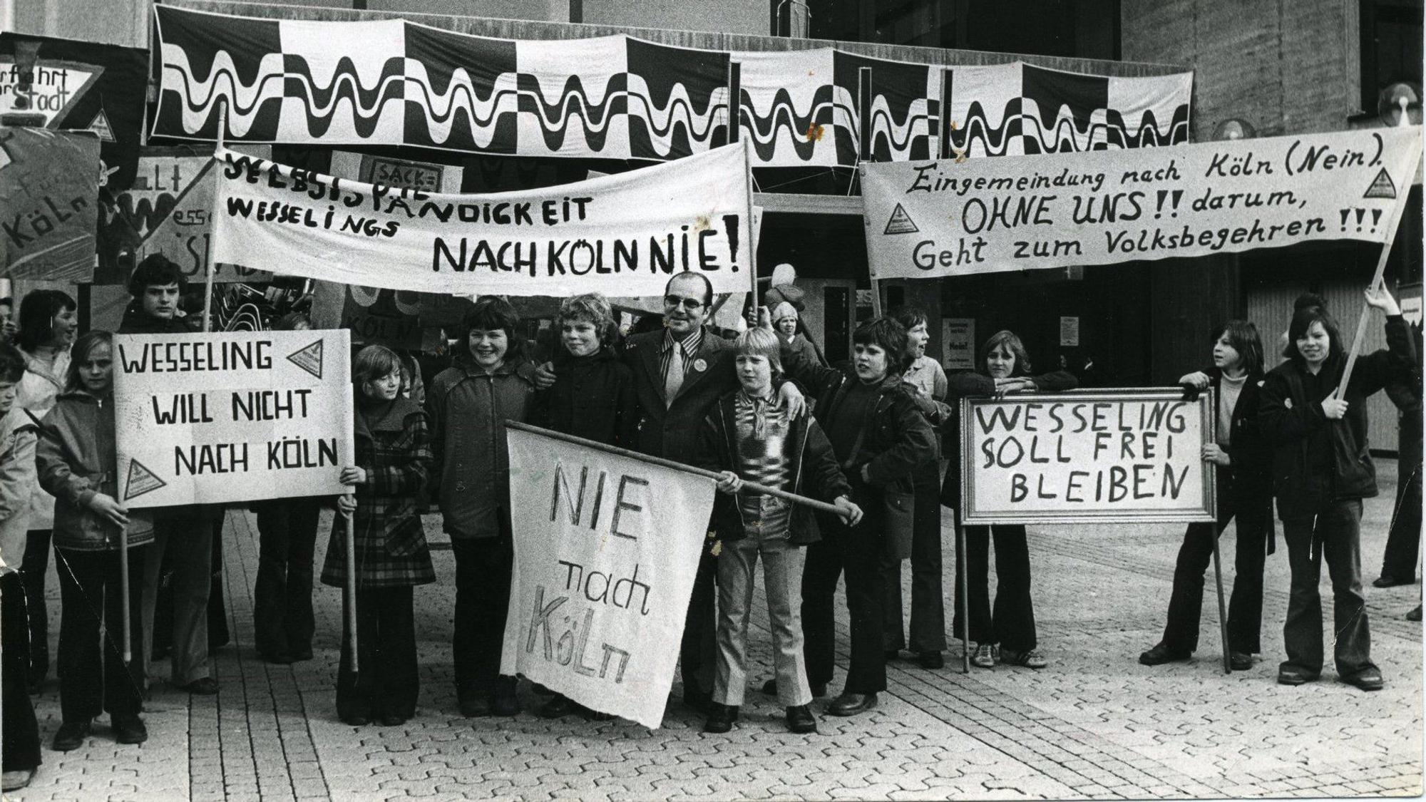 Auf dem Foto sind Wesselings Bürgermeister Martin Reglin und Schüler zu sehen. Sie demonstrieren vor dem Rathaus gegen die Eingemeindung ihrer Stadt nach Köln.