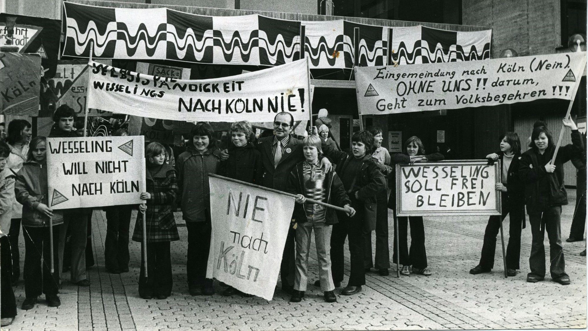 Auf dem Foto sind Wesselings Bürgermeister Martin Reglin und Schüler zu sehen. Sie demonstrieren vor dem Rathaus gegen die Eingemeindung ihrer Stadt nach Köln.
