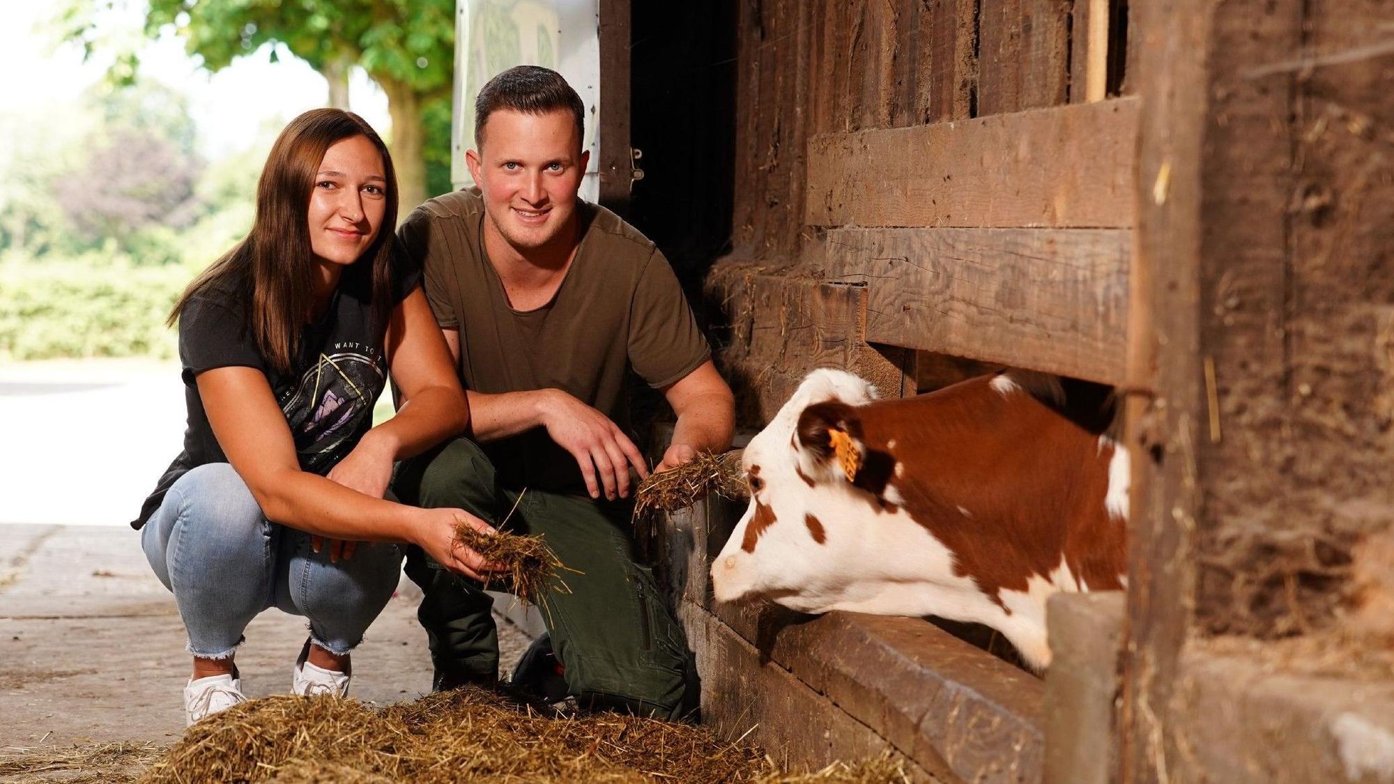 Bauer Patrick und Sarina knien im Stall vor einem Kalb.