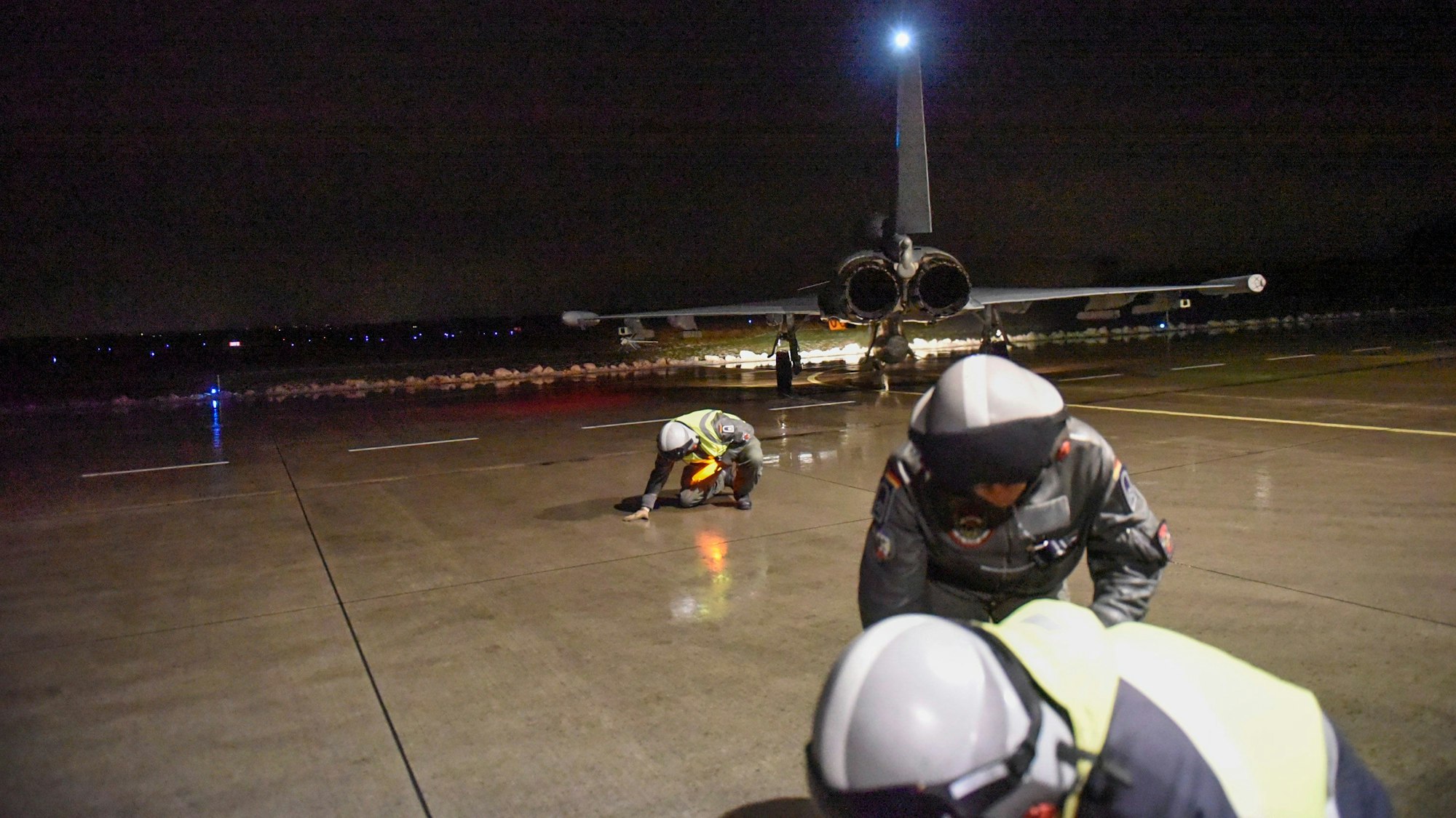 Techniker, die auf dem Rollfeld in Deckung gehen. Im Hintergrund ist ein Flugzeug zu sehen.