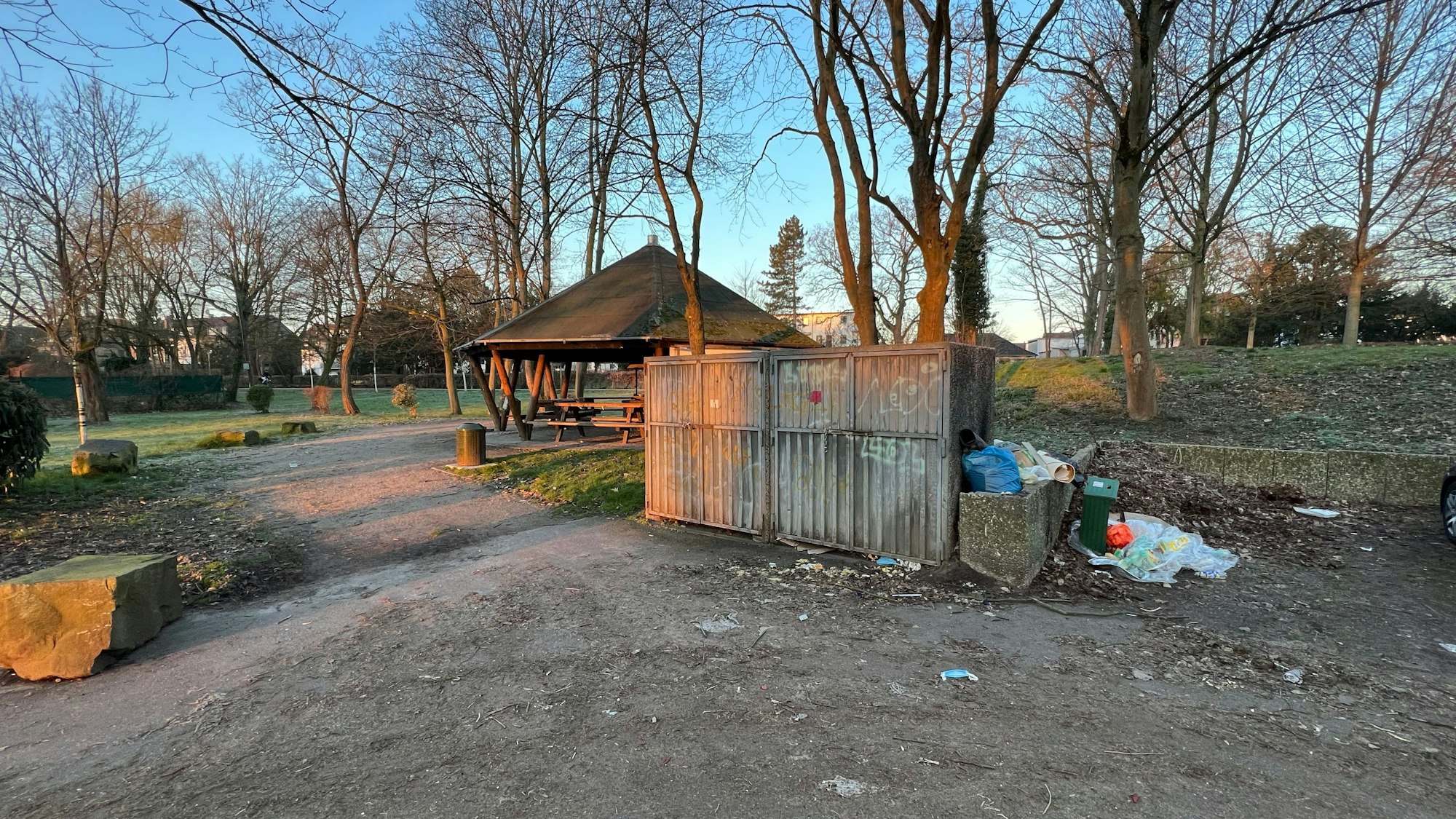 Im Umfeld einer Grillhütte, die auf einer Wiese mit Bäumen steht, ist Müll zu sehen.