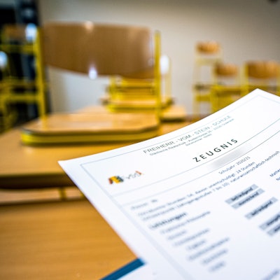 ARCHIV - 02.07.2021, Nordrhein-Westfalen, Gütersloh: Eine Klassenlehrerin hält das Zeugnis eines Schülers einer Schule in Gütersloh hoch. Bei Sorgen und Nöten rund ums Zeugnis schalten die fünf NRW-Bezirksregierungen auch in diesem Jahr wieder das Zeugnistelefon. Es dient dazu, eine «telefonische Rechtsberatung bei Fragen zu Noten und zur Schullaufbahn» zu liefern, wie die Bezirksregierungen mitteilen. (zu dpa: «Zeugnistelefone der Bezirksregierungen wieder erreichbar») Foto: David Inderlied/dpa +++ dpa-Bildfunk +++