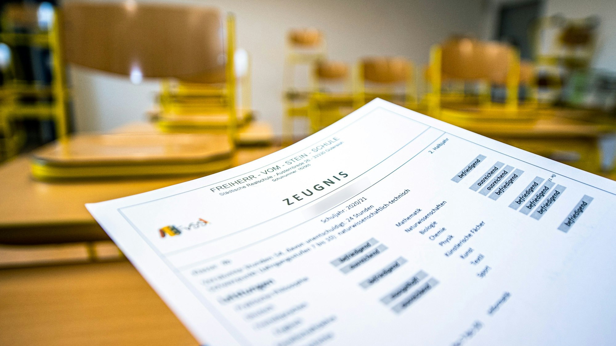 ARCHIV - 02.07.2021, Nordrhein-Westfalen, Gütersloh: Eine Klassenlehrerin hält das Zeugnis eines Schülers einer Schule in Gütersloh hoch. Bei Sorgen und Nöten rund ums Zeugnis schalten die fünf NRW-Bezirksregierungen auch in diesem Jahr wieder das Zeugnistelefon. Es dient dazu, eine «telefonische Rechtsberatung bei Fragen zu Noten und zur Schullaufbahn» zu liefern, wie die Bezirksregierungen mitteilen. (zu dpa: «Zeugnistelefone der Bezirksregierungen wieder erreichbar») Foto: David Inderlied/dpa +++ dpa-Bildfunk +++