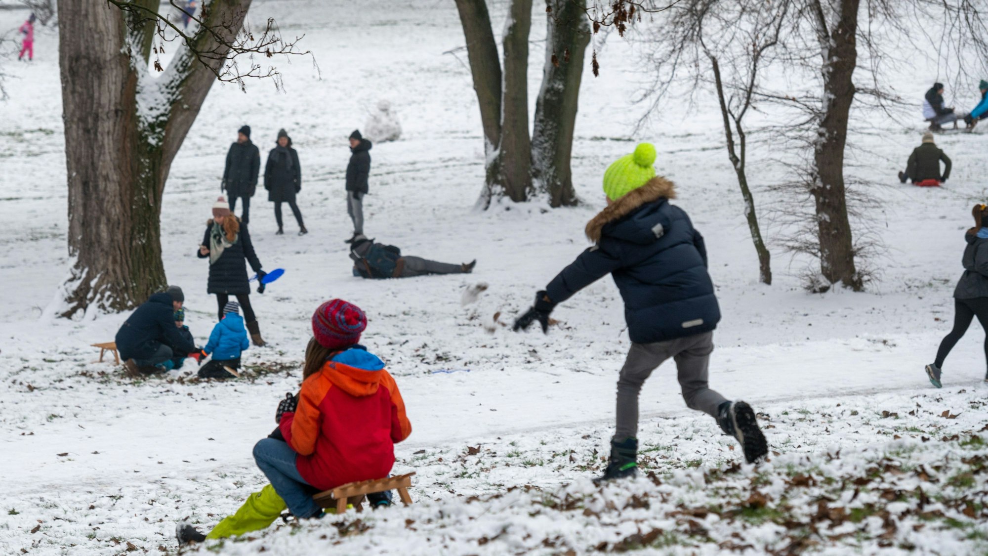 Zwei Kinder fahren den Hang hinunter, ein Junge rennt hinterher.