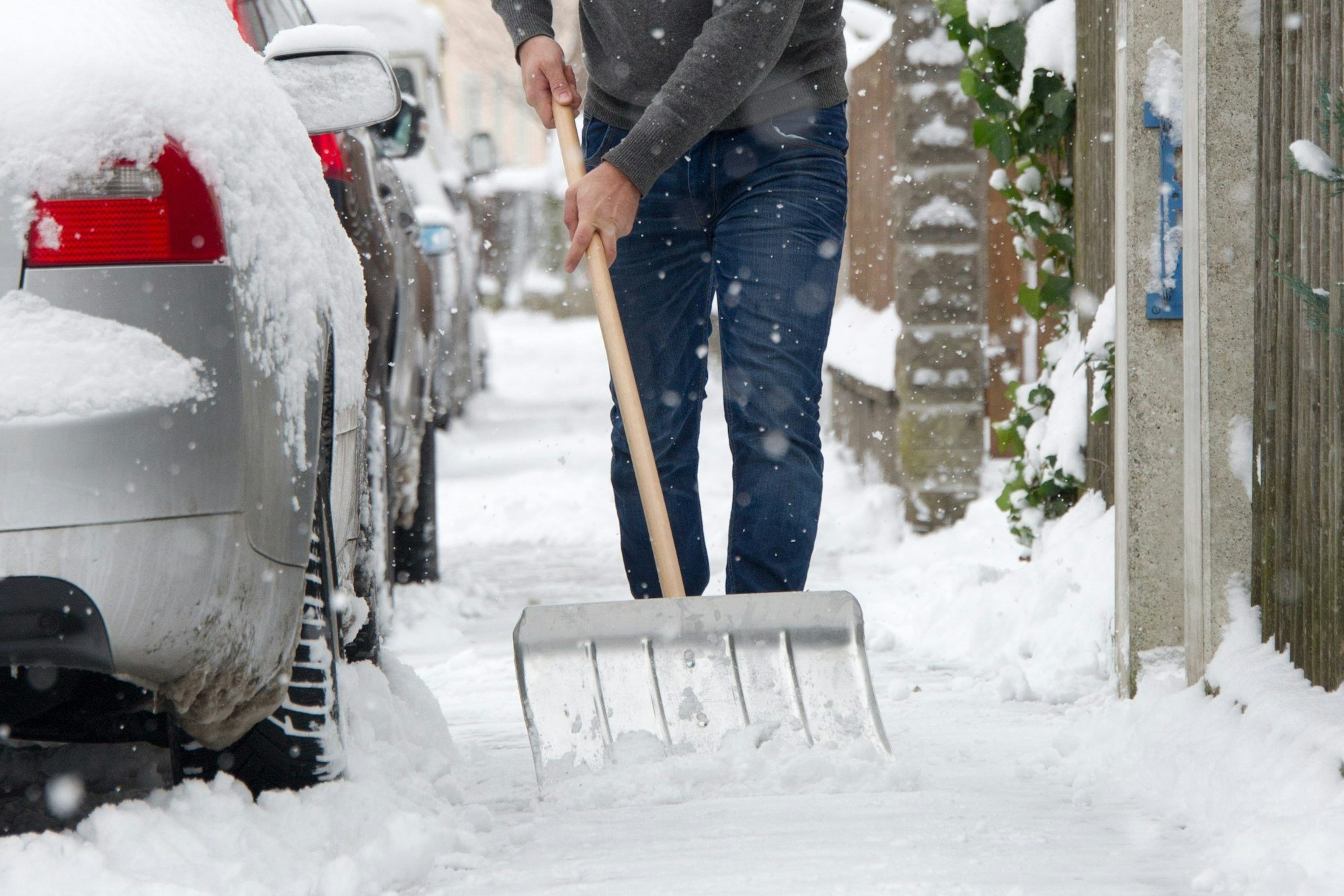 Ein Mann schippt Schnee auf einem Gehweg