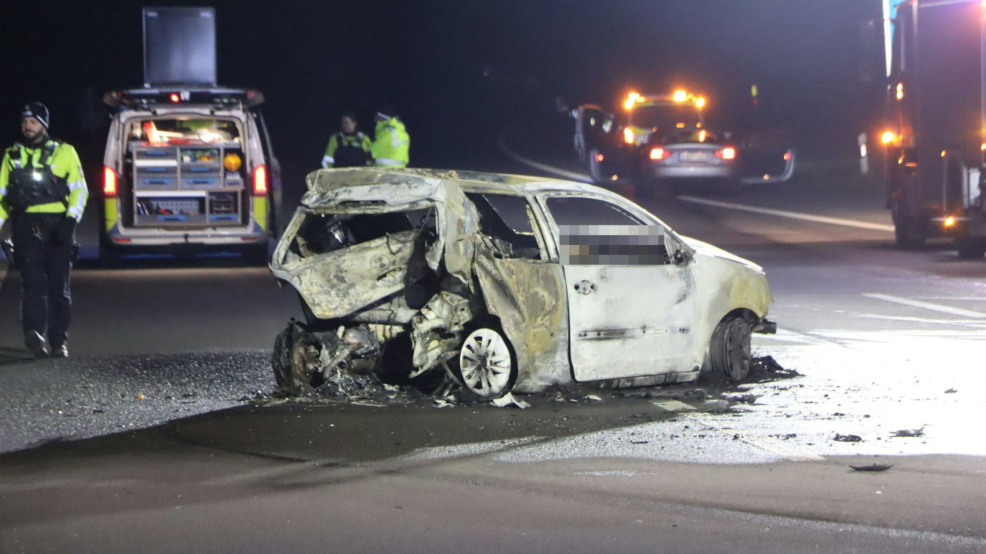 Einsatzkräfte stehen in der Nacht auf der Autobahn in der Nähe eines ausgebrannten VW-Polos. Die Autobahn, auf der der Wagen steht, ist komplett gesperrt.