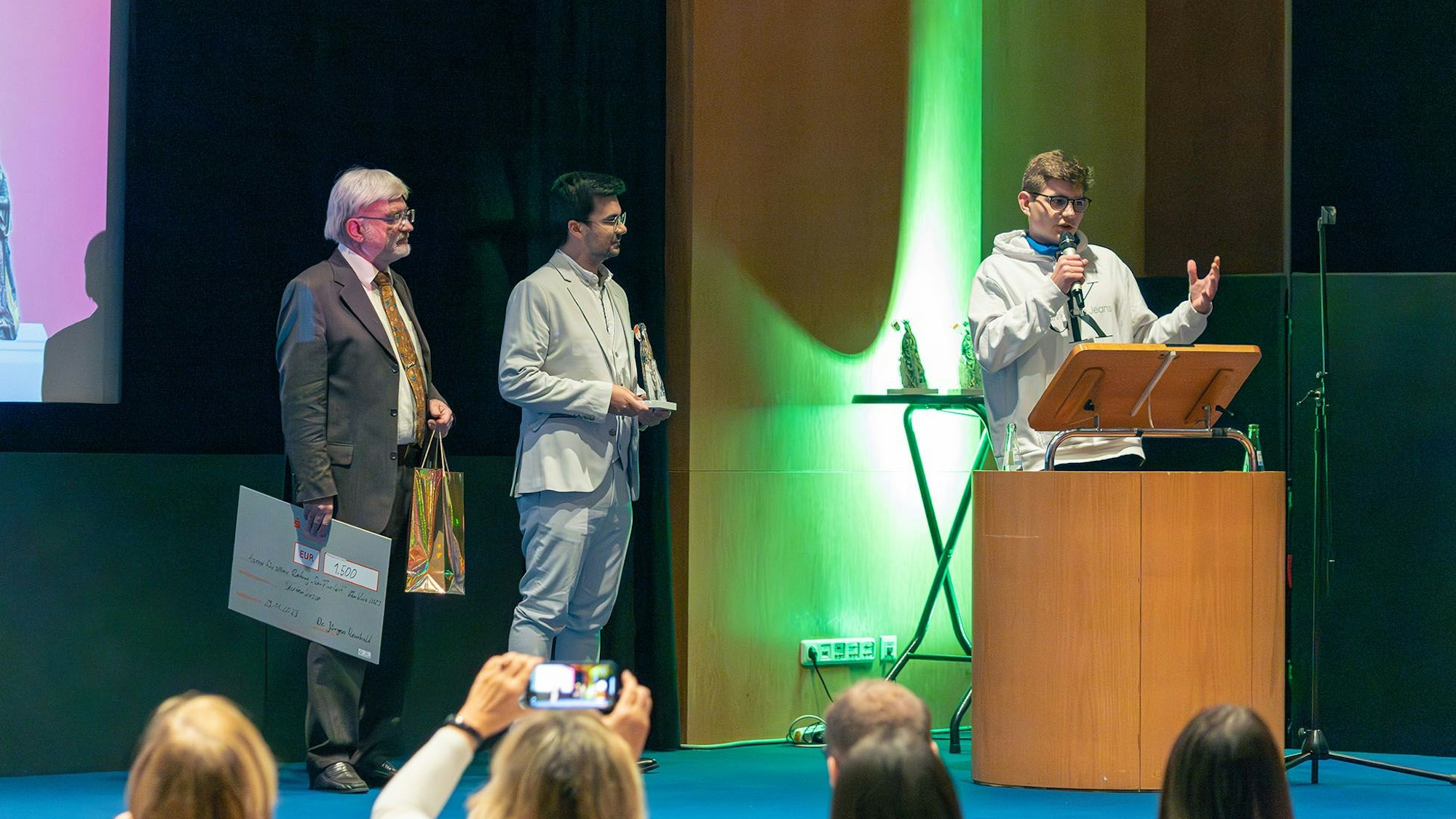 Publikumspreisträger Aaron am Mikro. Daneben stehen Dr. Rembold (links) und Üwen Ergün (Mitte)