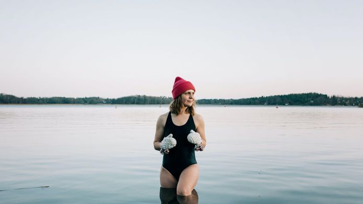 Auf dem Bild ist eine Frau mit Badeanzug, Mütze und Handschuhen zu sehen, die im See in der Eiszeit steht.