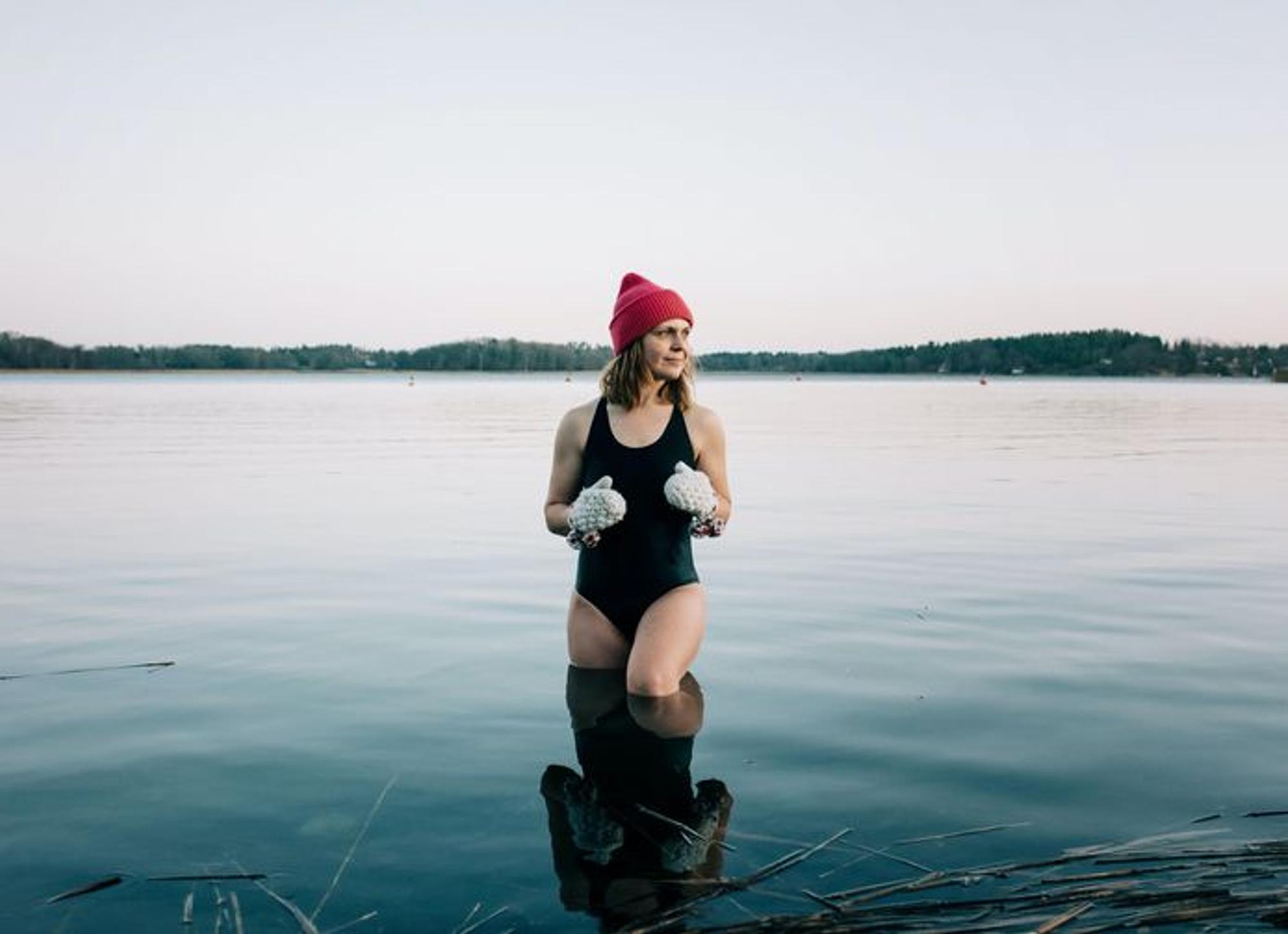 Auf dem Bild ist eine Frau mit Badeanzug, Mütze und Handschuhen zu sehen, die im See in der Eiszeit steht.