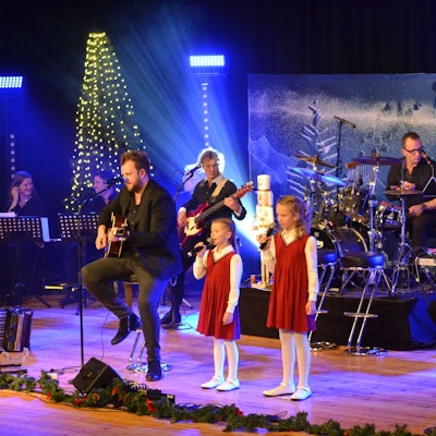 Romi und Lioli stehen in roten Kleidern mit den Paveiern auf der weihnachtlich geschmückten Bühne des Euskirchener Stadttheaters.