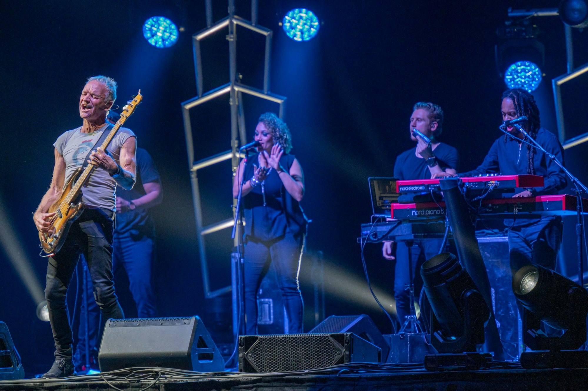 Sting steht links an der Bühne und singt, rechts Backroundsänger und Keyboarder