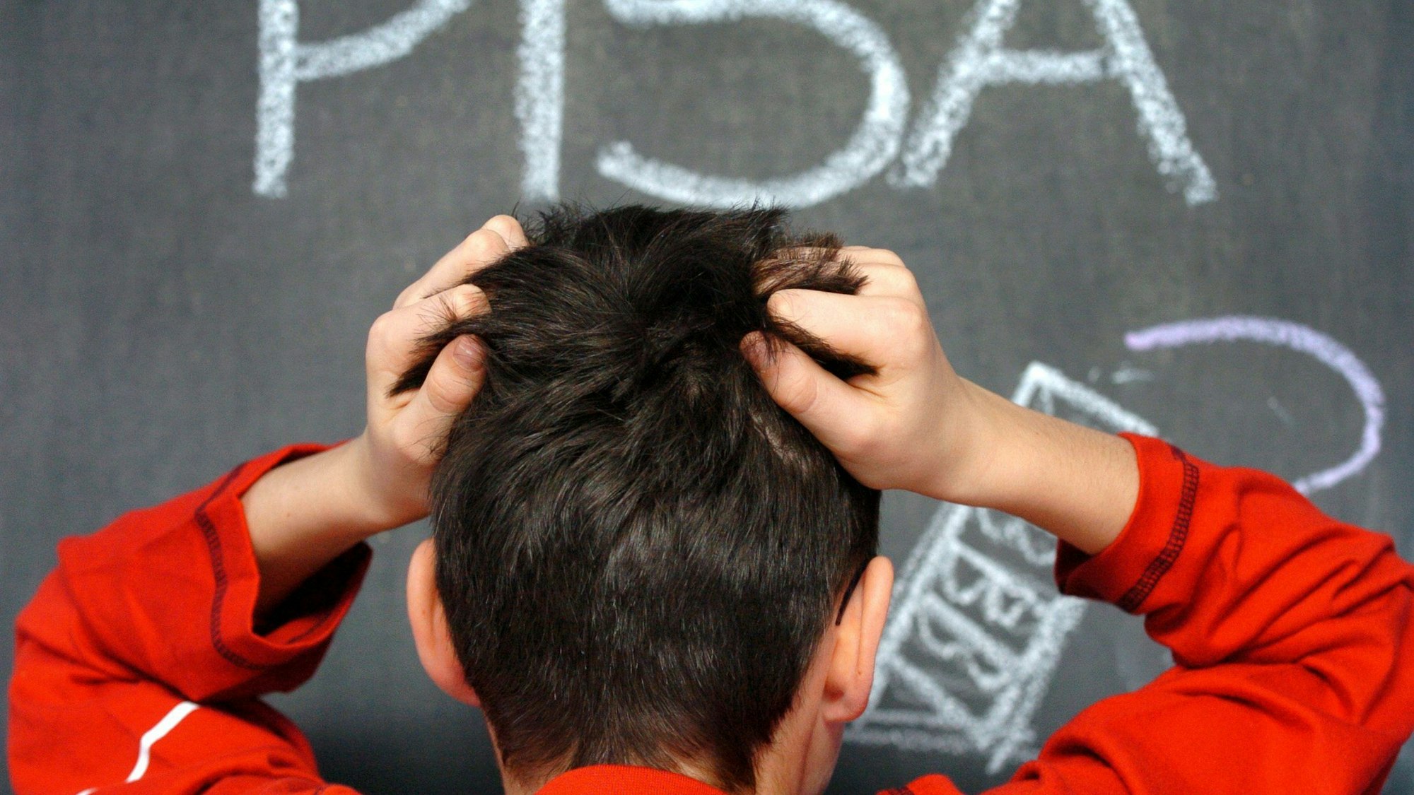 Ein Junge steht Haare raufend vor einer Tafel.