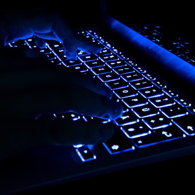 Ein Mann tippt in der Dunkelheit auf erleuchtete Tasten eines Laptops.