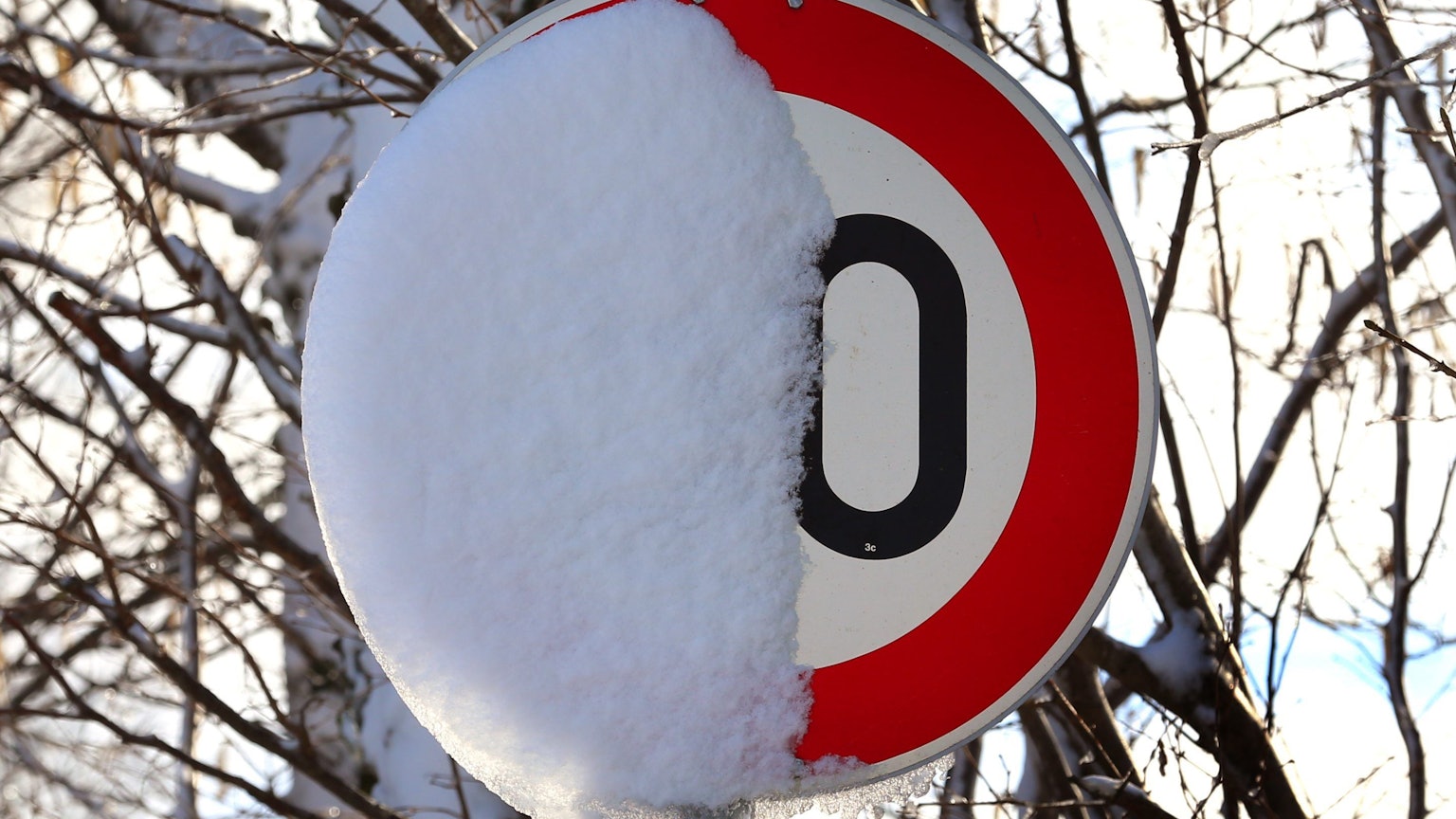 Ein Schild, das auf ein Tempolimit hinweist, ist halb zugeschneit. Die Zahl ist deshalb nicht zu erkennen.