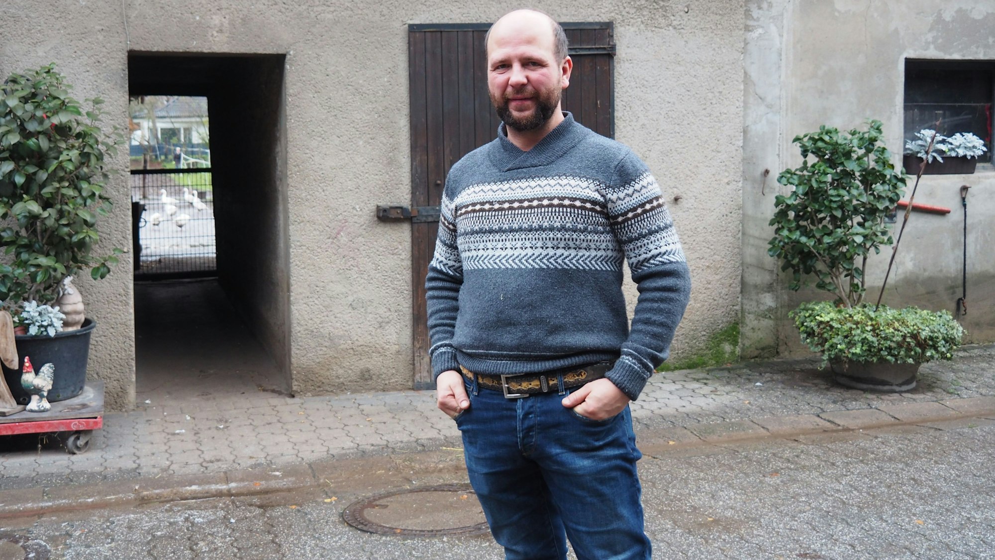 Ein Mann mit Bart steht im Hof eines Bauernhofs.