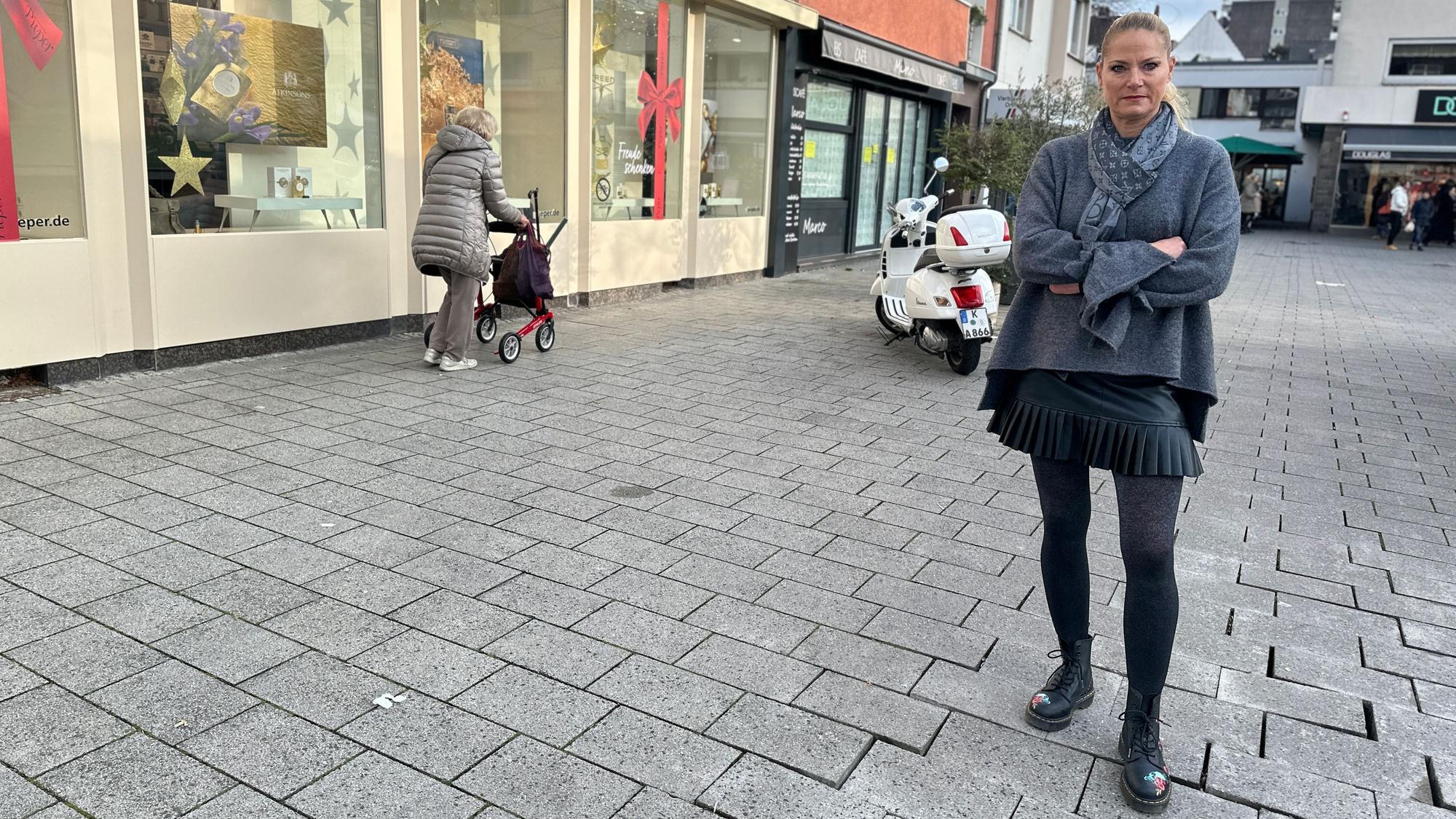 Eine Frau steht auf einem Platz, die Pflastersteine sind zum Teil schief.