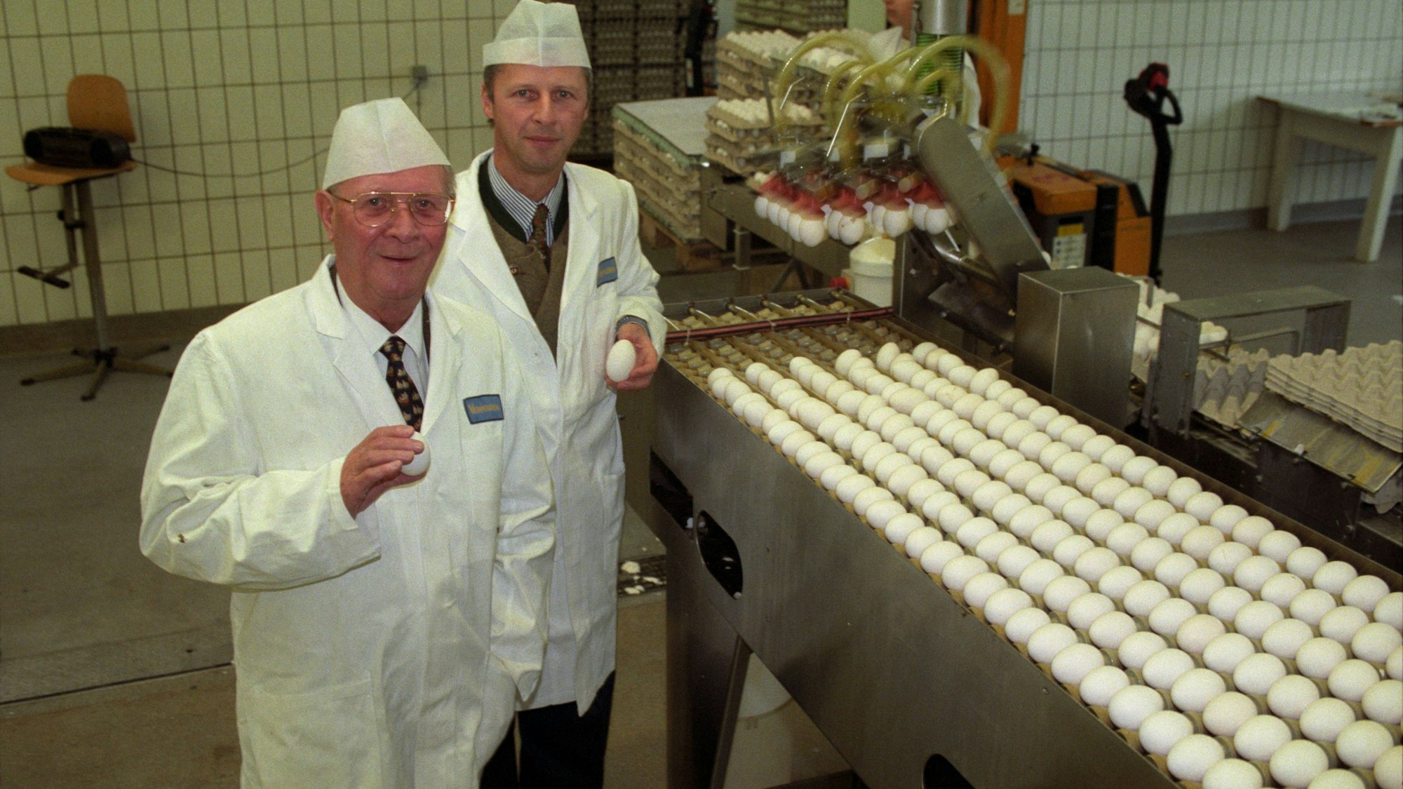 Eierlikörfabrikant Viktor Verpoorten (l.) mit seinem Sohn William im Unternehmenssitz der Verpoorten GmbH & Co. KG in Bonn in 1999. Sie stehen, in weißen Arbeitskitteln gekleidet, neben einer Produktionsanlage, auf der sich zig Eier befinden.