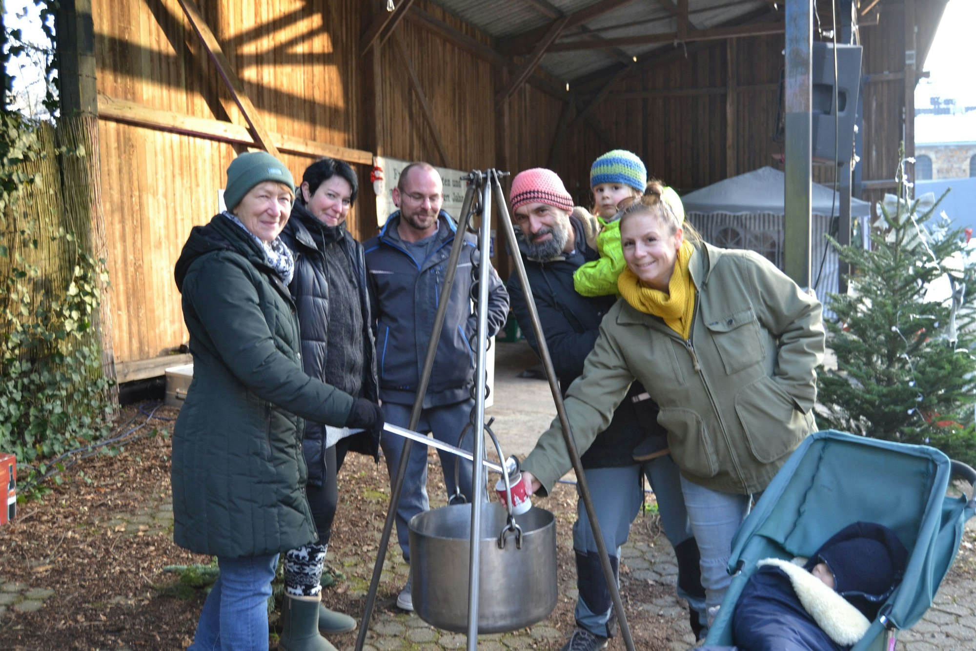 Eine Gruppe Menschen steht um einen Kessel an einem Tripod und halten Tassen in Händen.