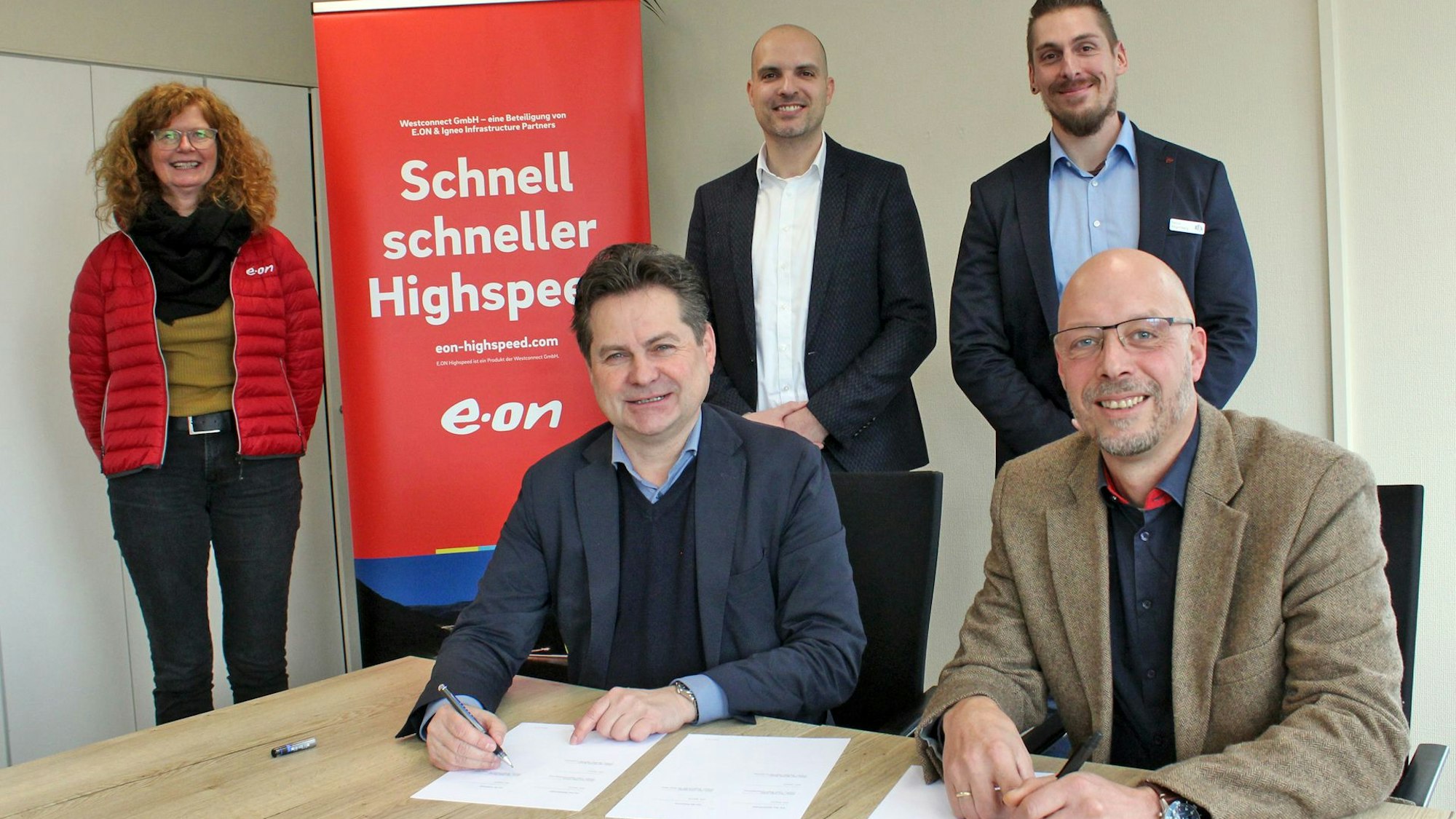 Zwei Herren am Tisch, dahinter stehend drei weitere Personen.