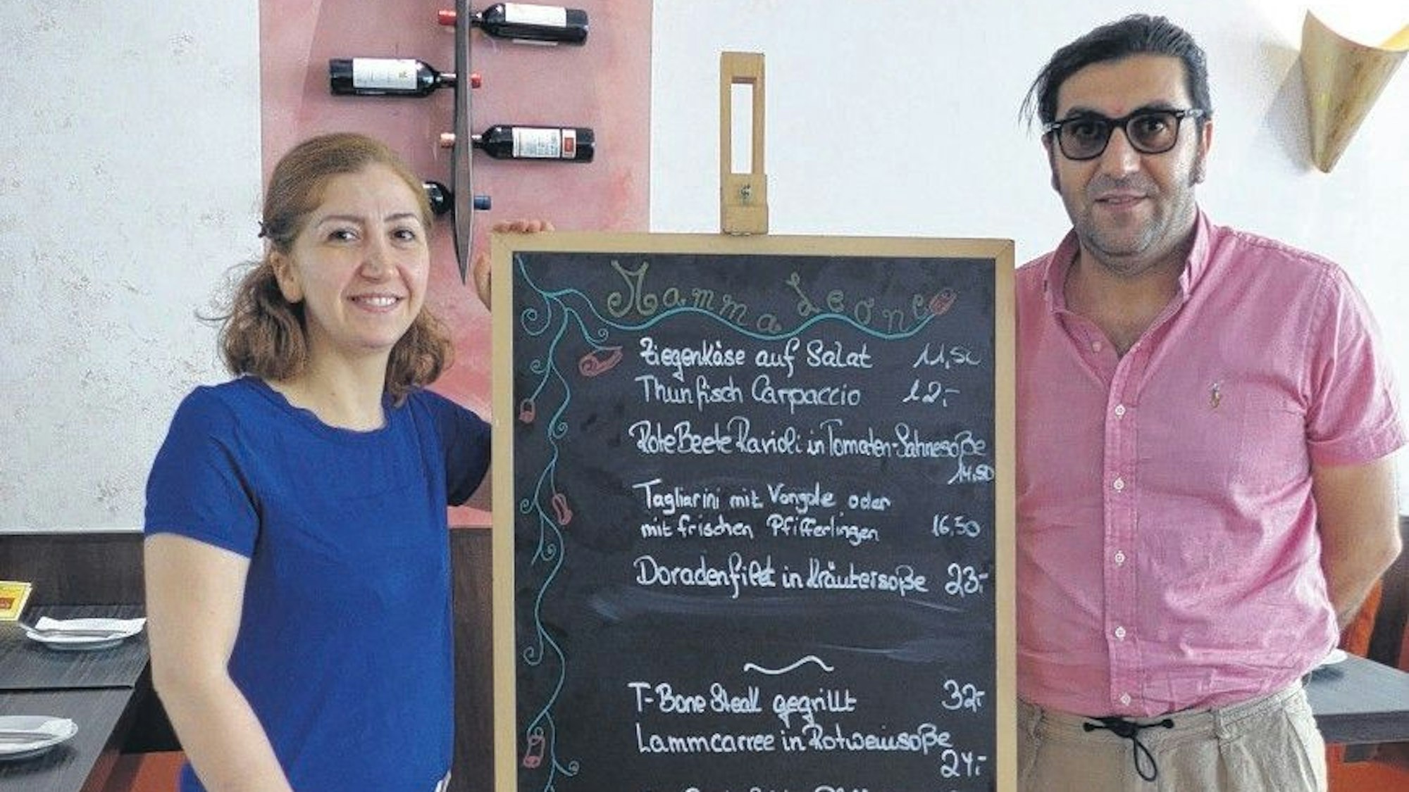 Das Foto zeigt Sabu Senol und ihren Mann Tahir vor einer Tafel mit Tagesgerichten.