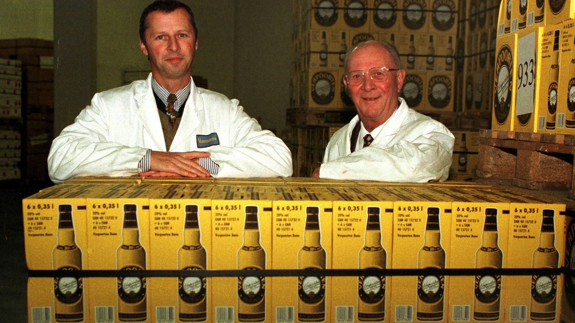 William Verpoorten (l.) und sein Sohn William lehnen auf Kisten gefüllt mit Flaschen ihres Eierlikörs. Sie lächeln beide in die Kamera.
