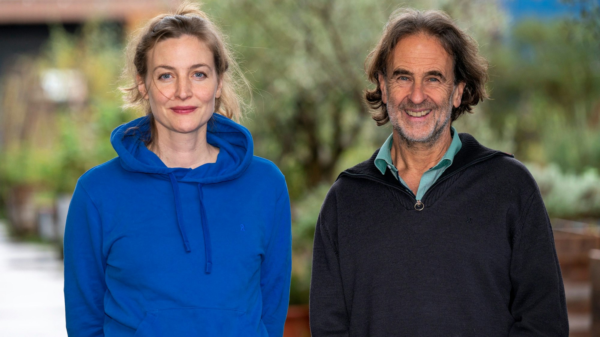 Schauspielerin Ines Marie Westernströer trägt einen blauen Hoodie, Friedhelm Friebe einen dunkelblauen Pullover über grünem Hemd. Beide lächeln.