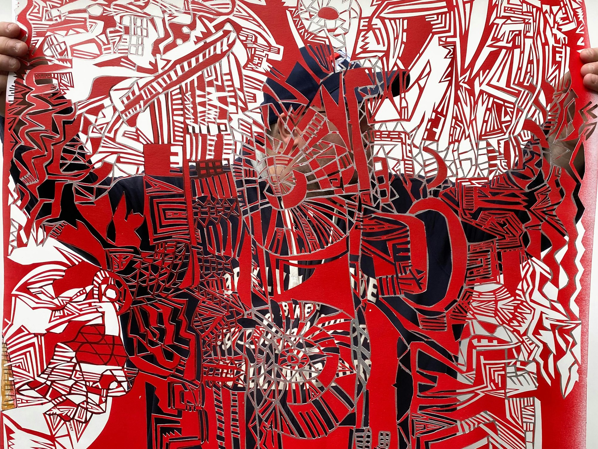 Markus Schmitz zeigt seinen Scherenschnitt auf rotem Papier. Er selbst steht dahinter.