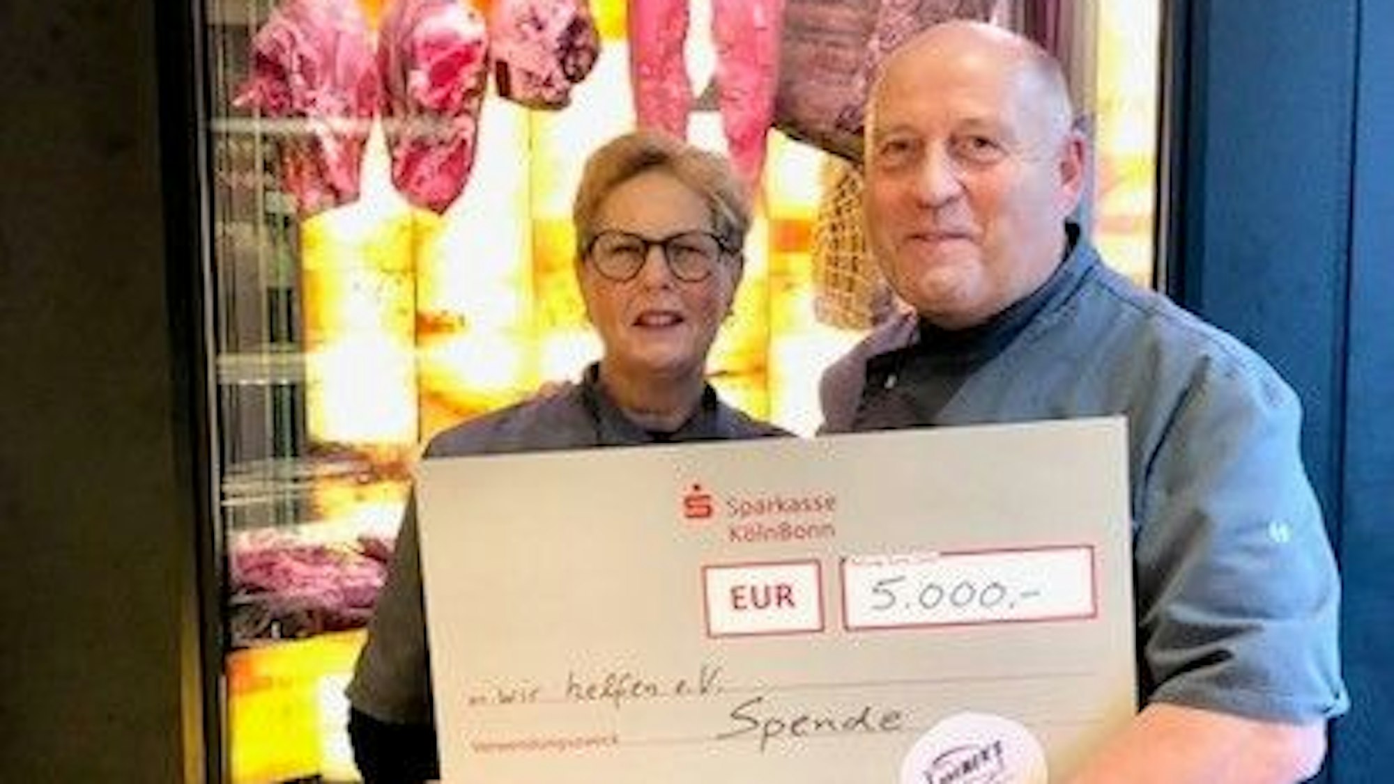 Gertrud und Thomas Kremers stehen mit einem symbolischen Scheck über 5.000 Euro vor einer Fleischtheke