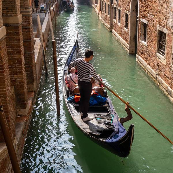 Ein Gondoliere steuert eine Gondel mit Touristen durch einen Kanal. (Symbolbild)