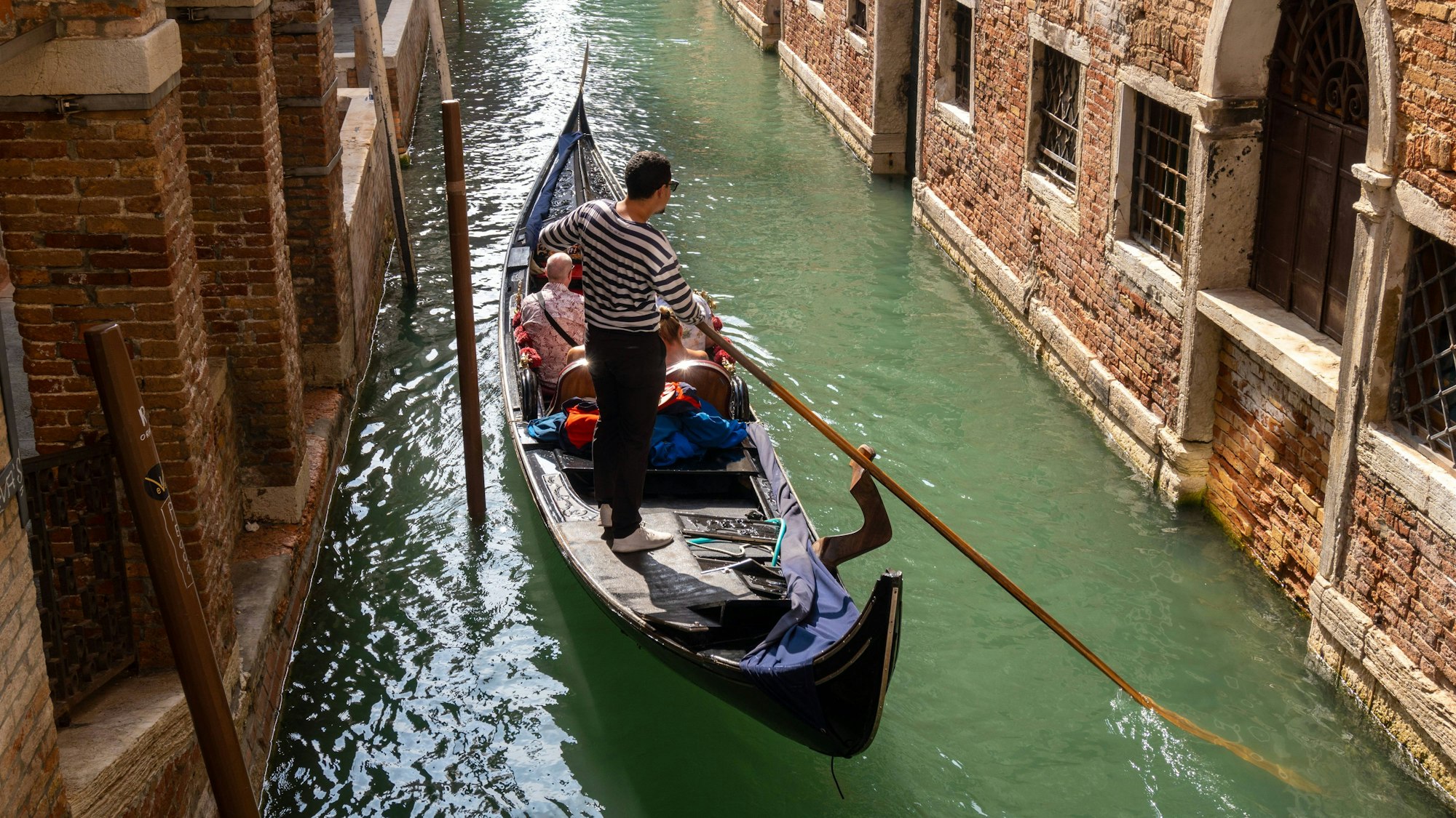 Ein Gondoliere steuert eine Gondel mit Touristen durch einen Kanal. (Symbolbild)