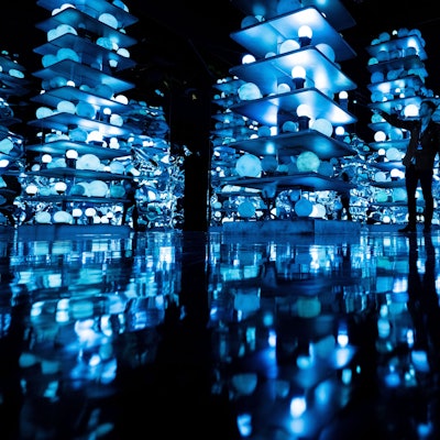 Ein Mann steht in einem dunklen Raum voller Glaskugeln in Regalen, die blau leuchten.