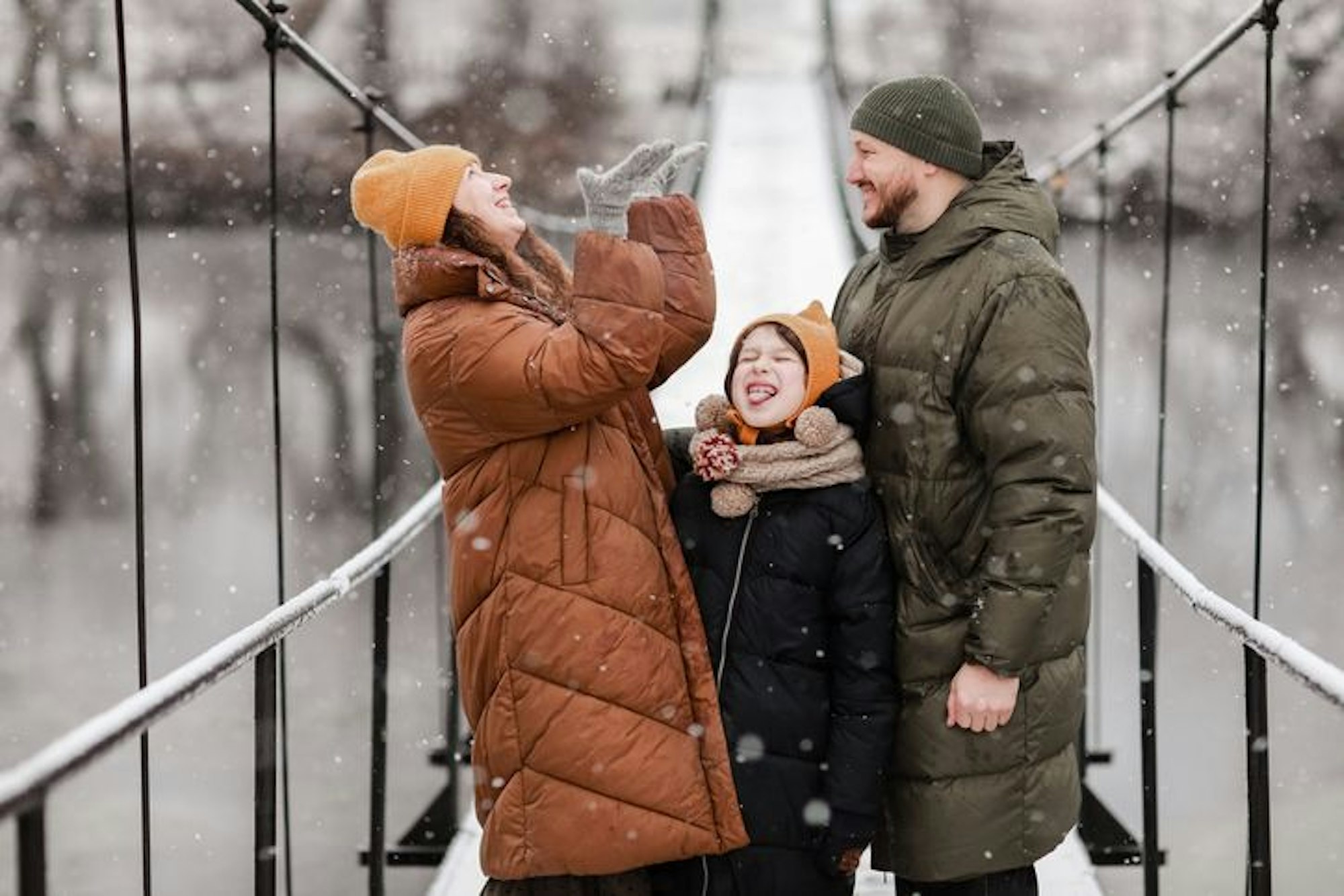 Young mother, father and the little daughter catches snowflakes in a beautiful winter park during a snowfall. It is snowing. family is playing in the snow. Winter activities. the winter holidays