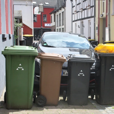 Eine Papiertonne, eine Biotonne, eine Restmülltonne und eine Wertstofftonne der RSAG stehen nebeneinander abholbereit auf einer Straße in Siegburg.