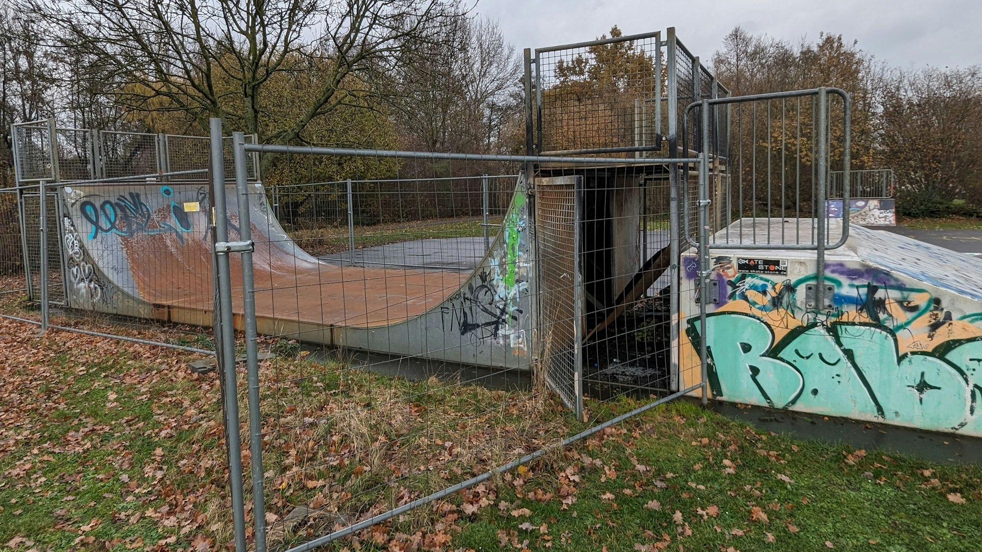 Eine mit Graffiti versehene Halfpipe für Skater hinter einem Bauzaun.