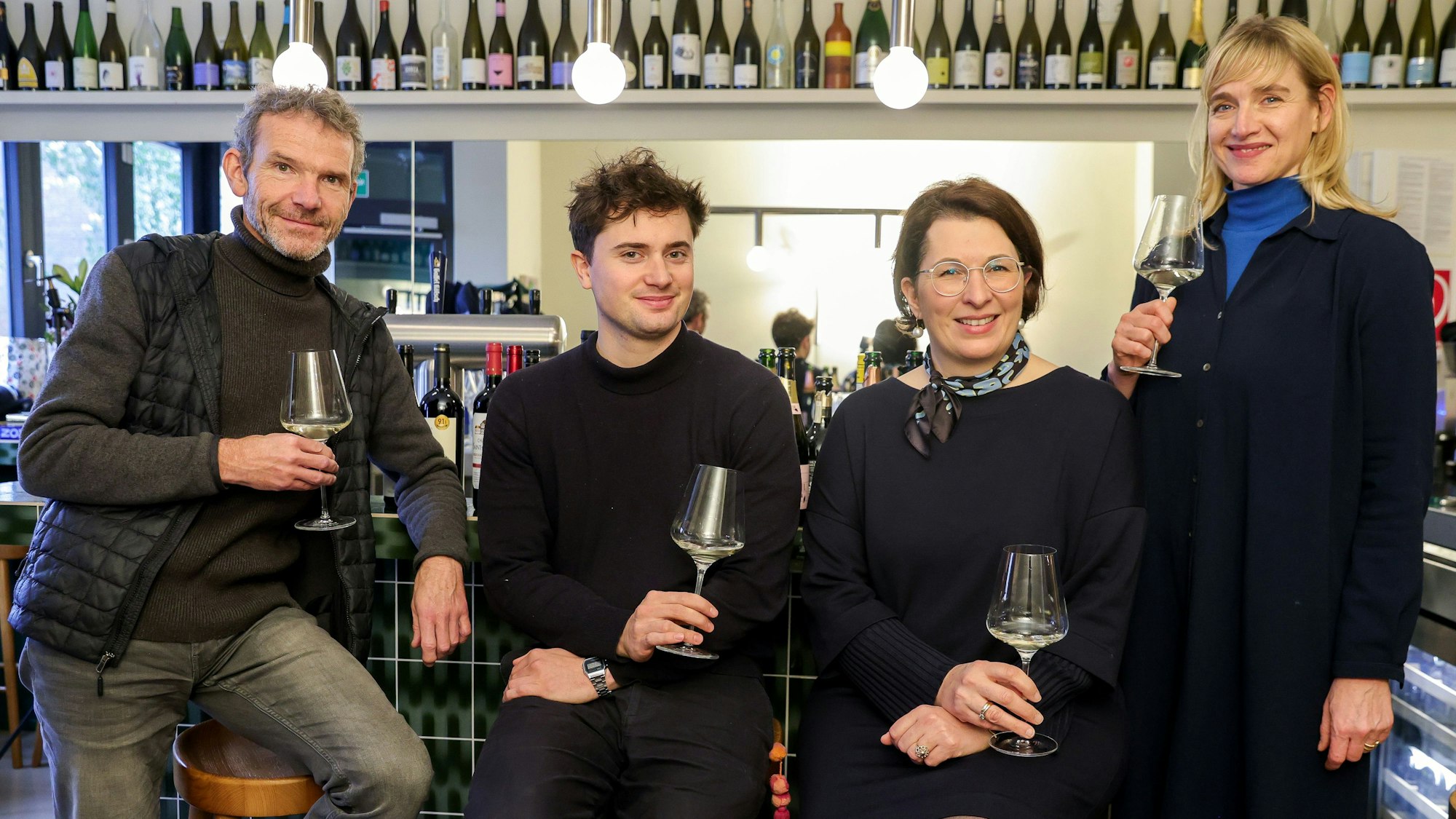 Vier Menschen stehen mit einem Glas Wein in der Hand an einem Kneipentresen.