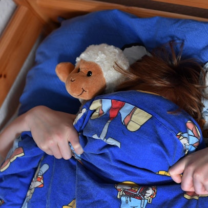 Ein zehnjähriger Junge hat sich seine Bettdecke über das Gesicht gezogen.