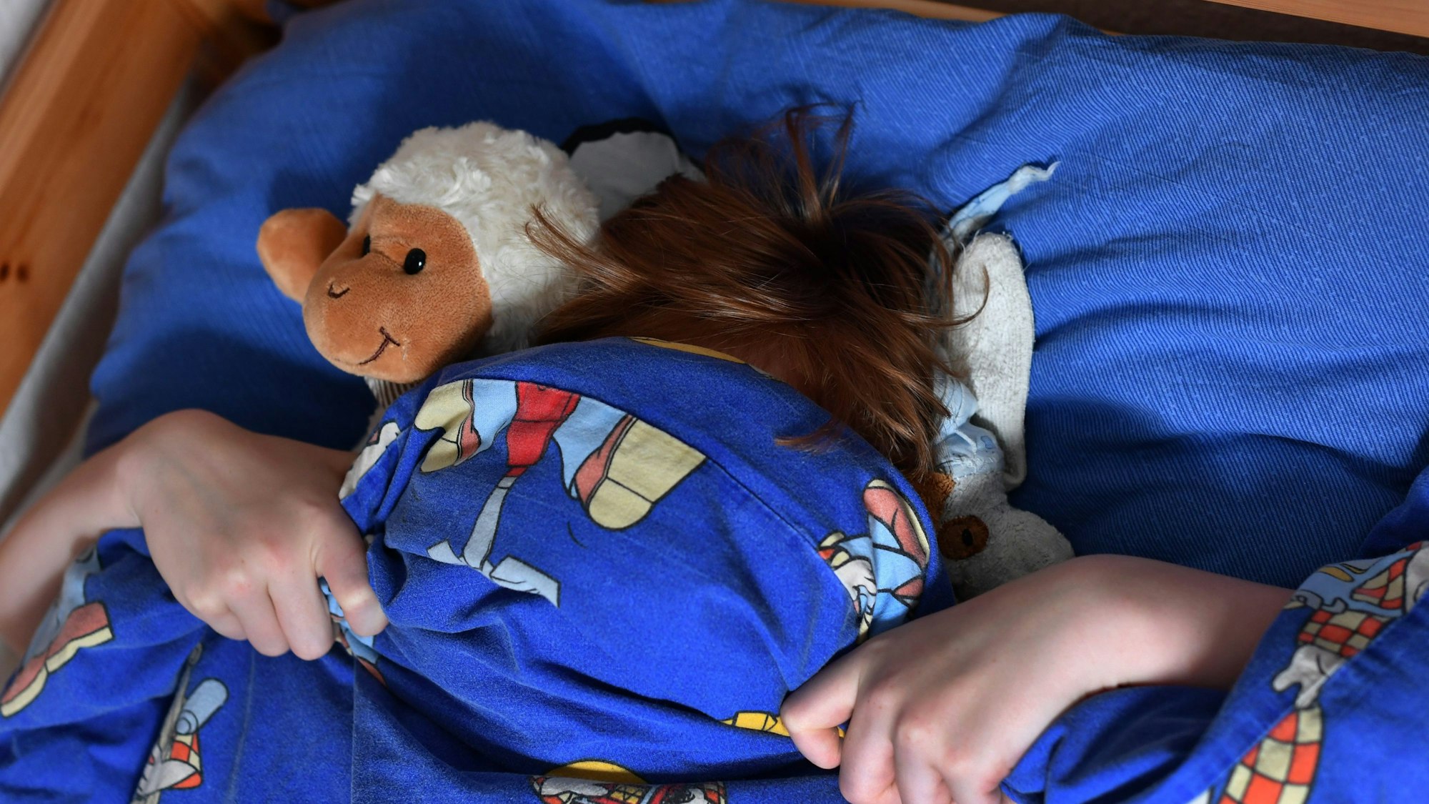 Ein zehnjähriger Junge hat sich seine Bettdecke über das Gesicht gezogen.