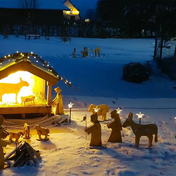 Eine beleuchtete Weihnachtskrippe mit Holzfiguren steht auf einer verschneiten Wiese in Ripsdorf.