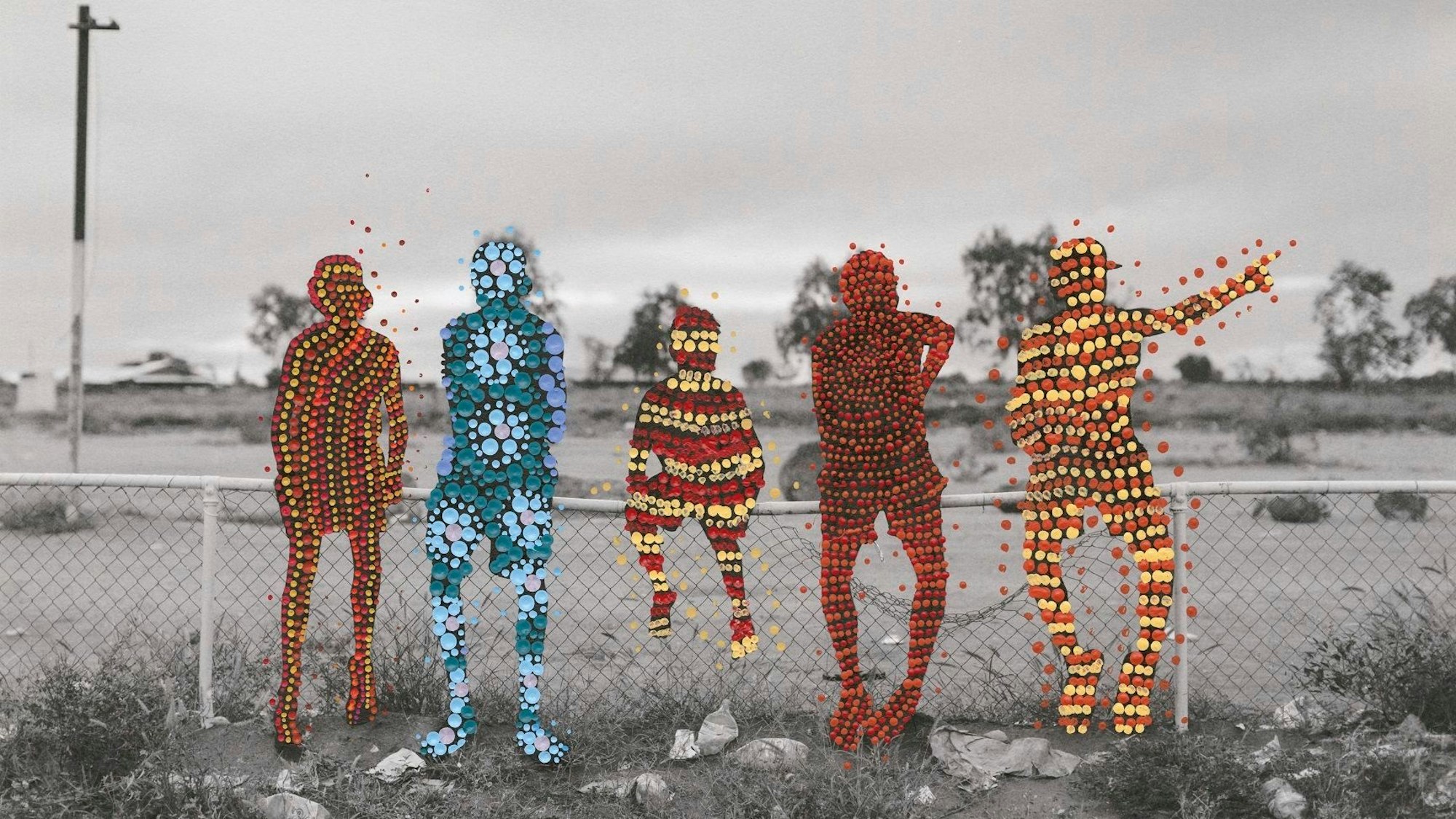 Die Schwarz-Weiß-Fotografie zeigt fünf Personen der australischen Warlpiri, auf einem Zaun sitzend, sie sind von zwei Warlpiri-Künstlerinnen mit tradierten Mustern übermalt worden.