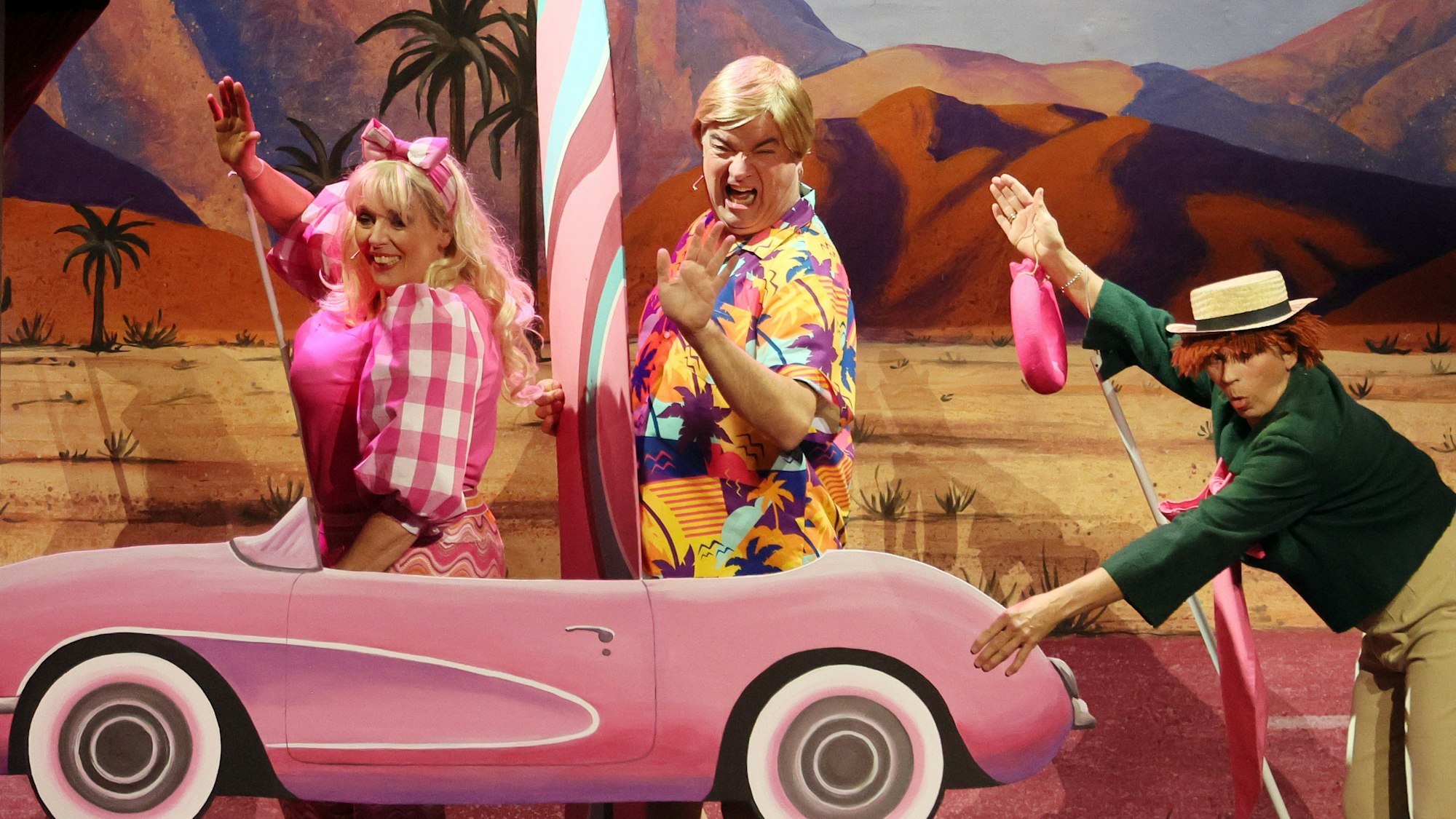 Anna Rixmann, Tom Simon und Martina Klinke als Hänneschen-Figuren in Barbie-Version mit einem pinkfarbenen Papp-Auto.