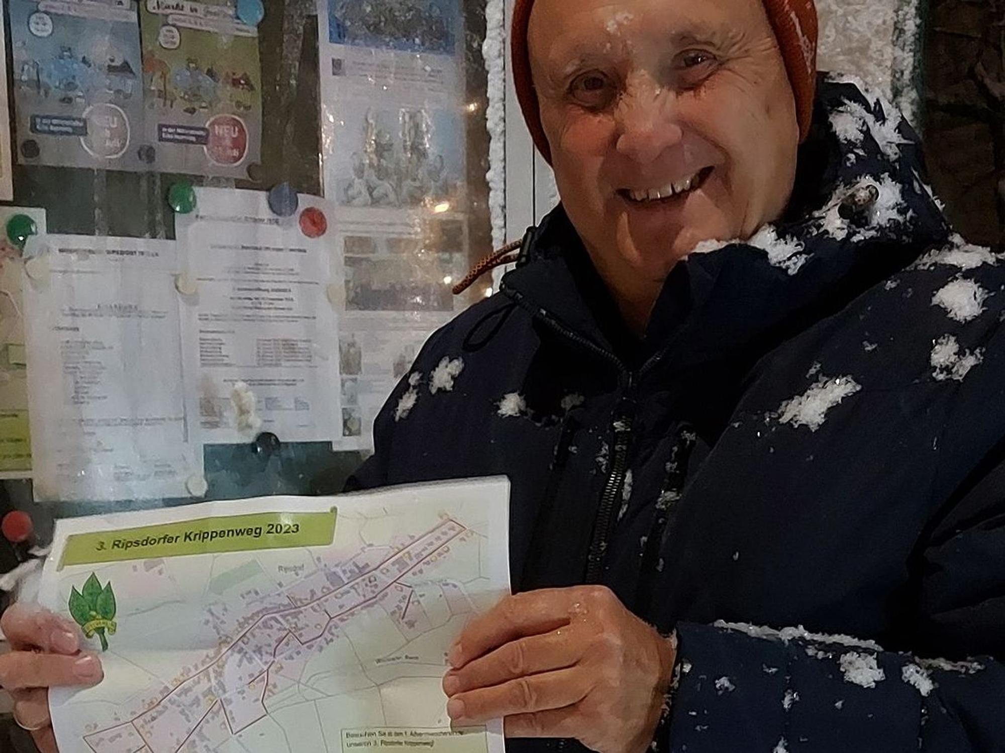 Herbert Peetz steht im Schneetreiben. Er hält einen Lageplan zum Krippenweg in Ripsdorf in der Hand.