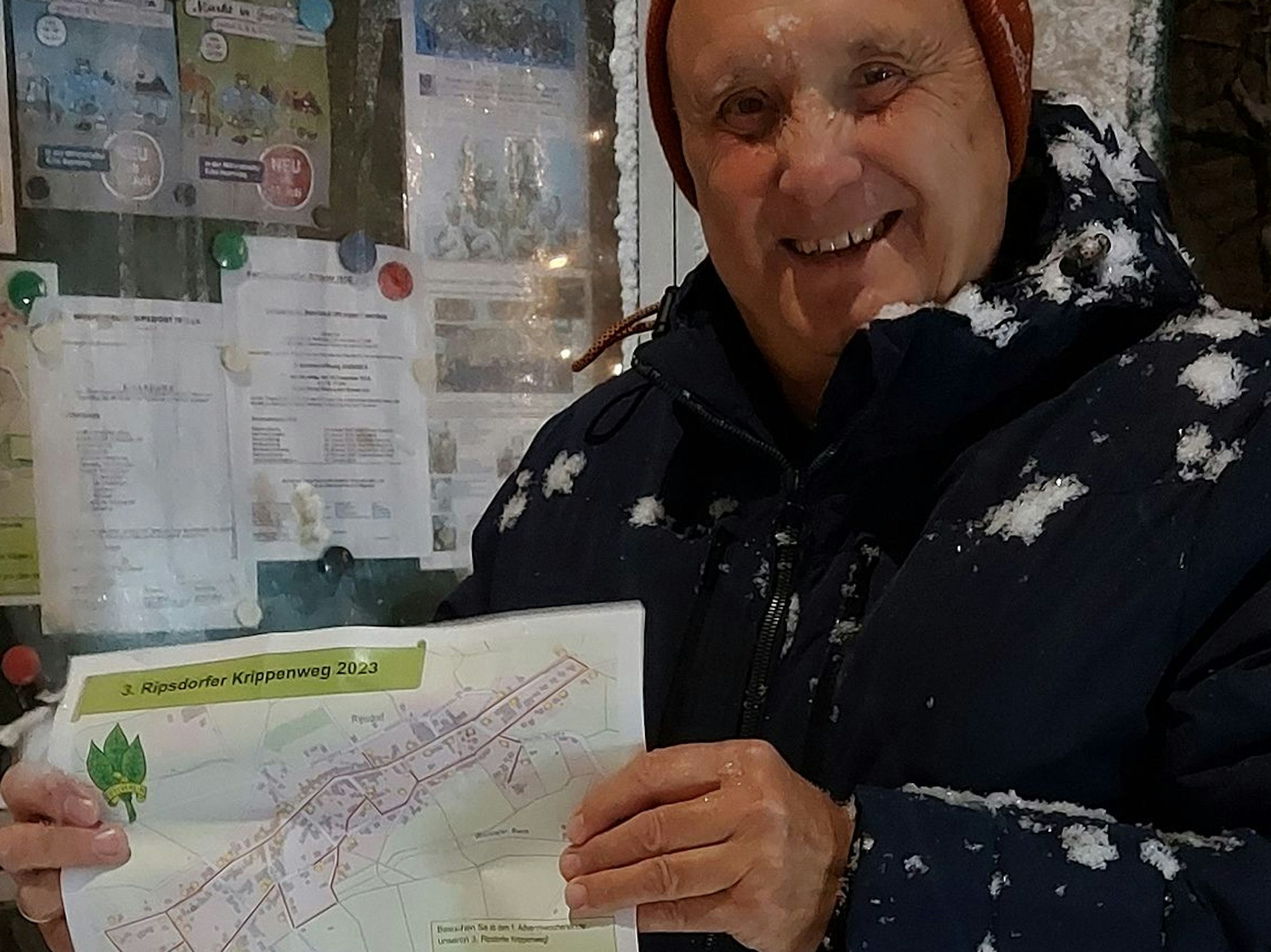Herbert Peetz steht im Schneetreiben. Er hält einen Lageplan zum Krippenweg in Ripsdorf in der Hand.