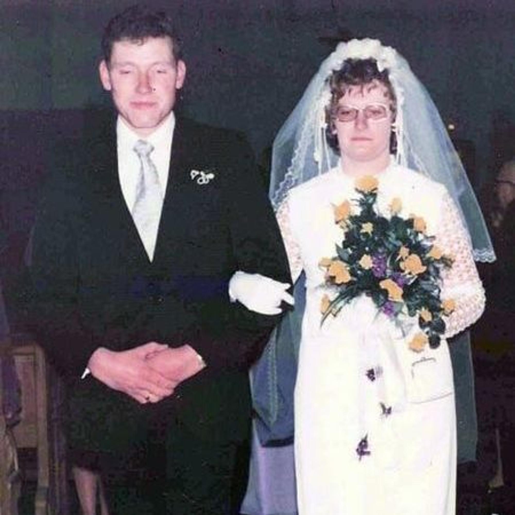 Das Bild zeigt das Ehepaar Breuer bei seiner Hochzeit: Maria Breuer trägt ein Brautkleid und hält einen gelb-violetten Blumenstrauß in den Händen. Franz-Josef Breuer in einem schwarzen Anzug.