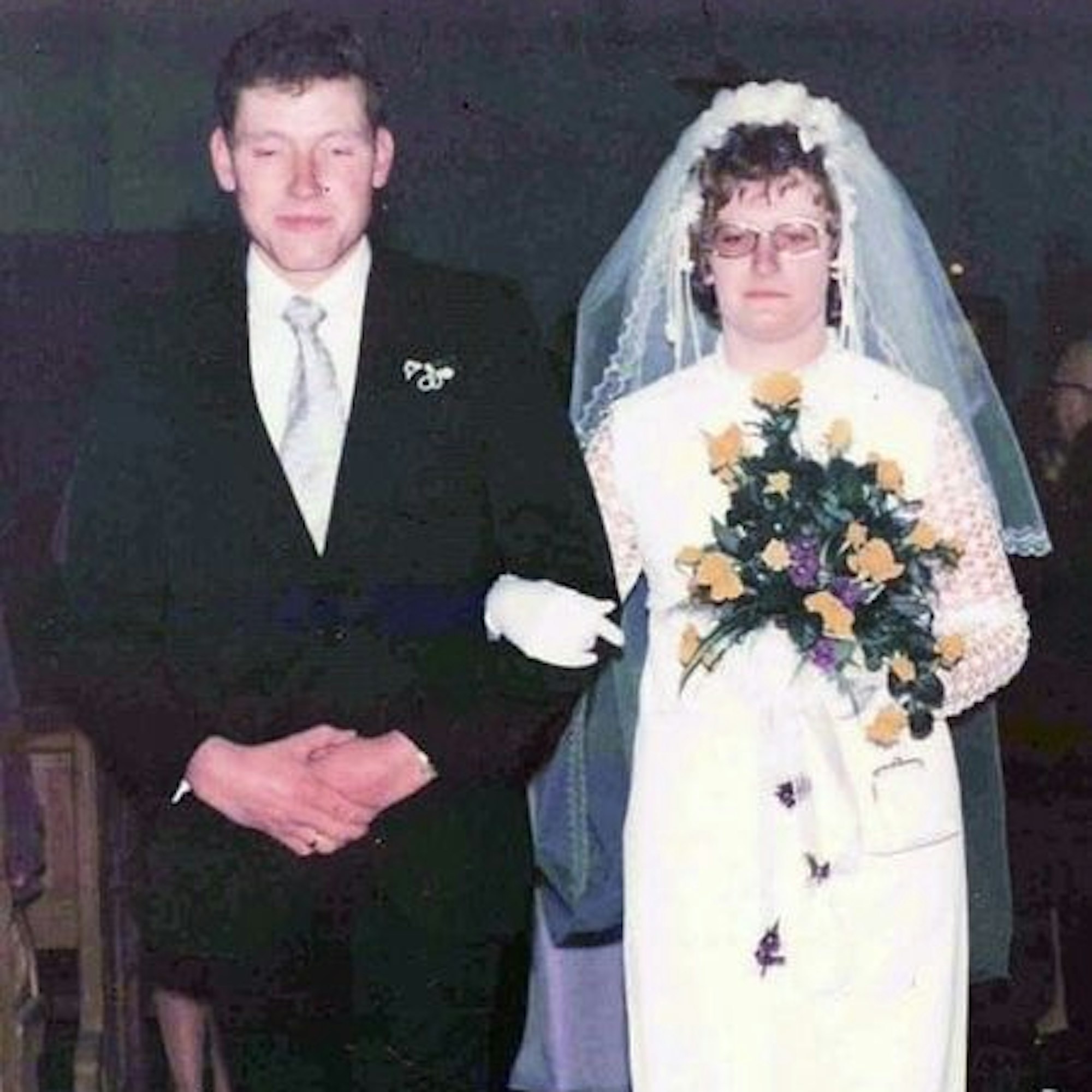 Das Bild zeigt das Ehepaar Breuer bei seiner Hochzeit: Maria Breuer trägt ein Brautkleid und hält einen gelb-violetten Blumenstrauß in den Händen. Franz-Josef Breuer in einem schwarzen Anzug.